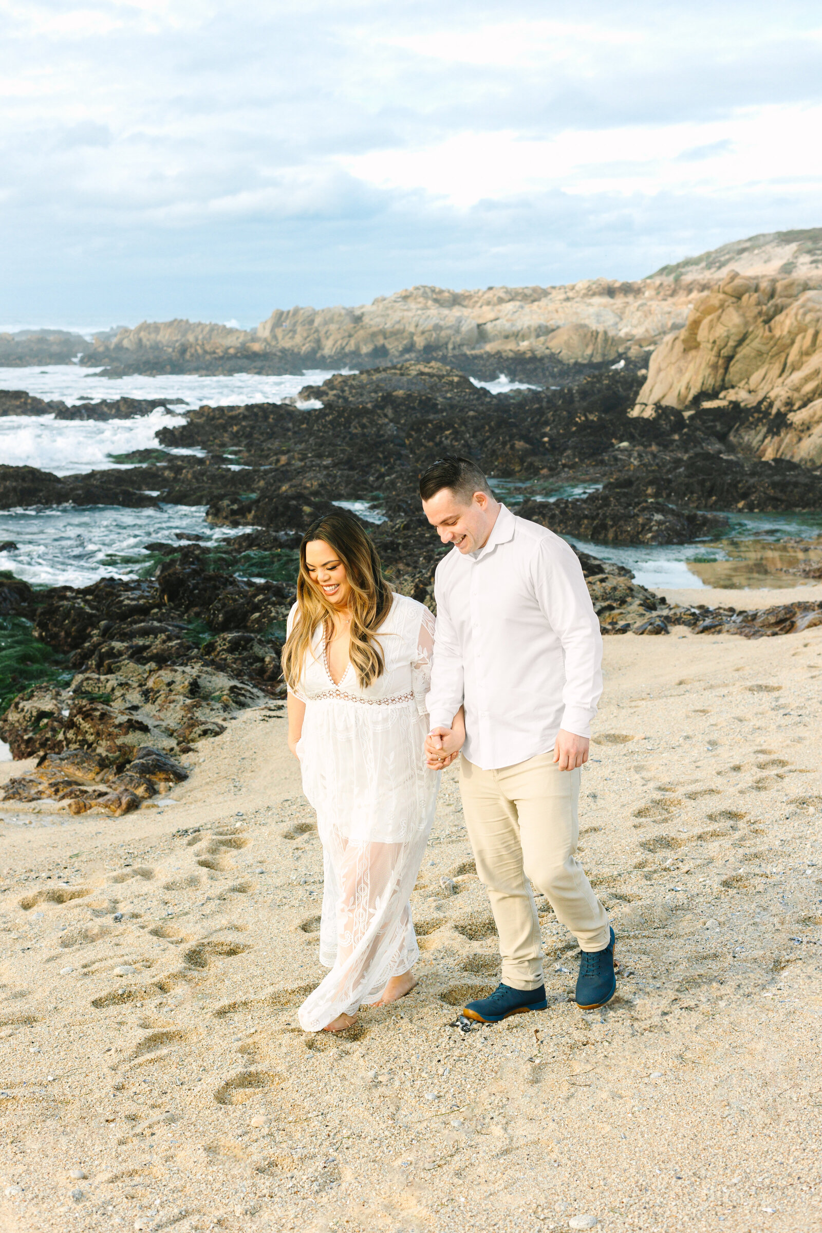 An engaged man and woman take photos on the beach in Pacific Grove, Monterey, California near Big Sur.