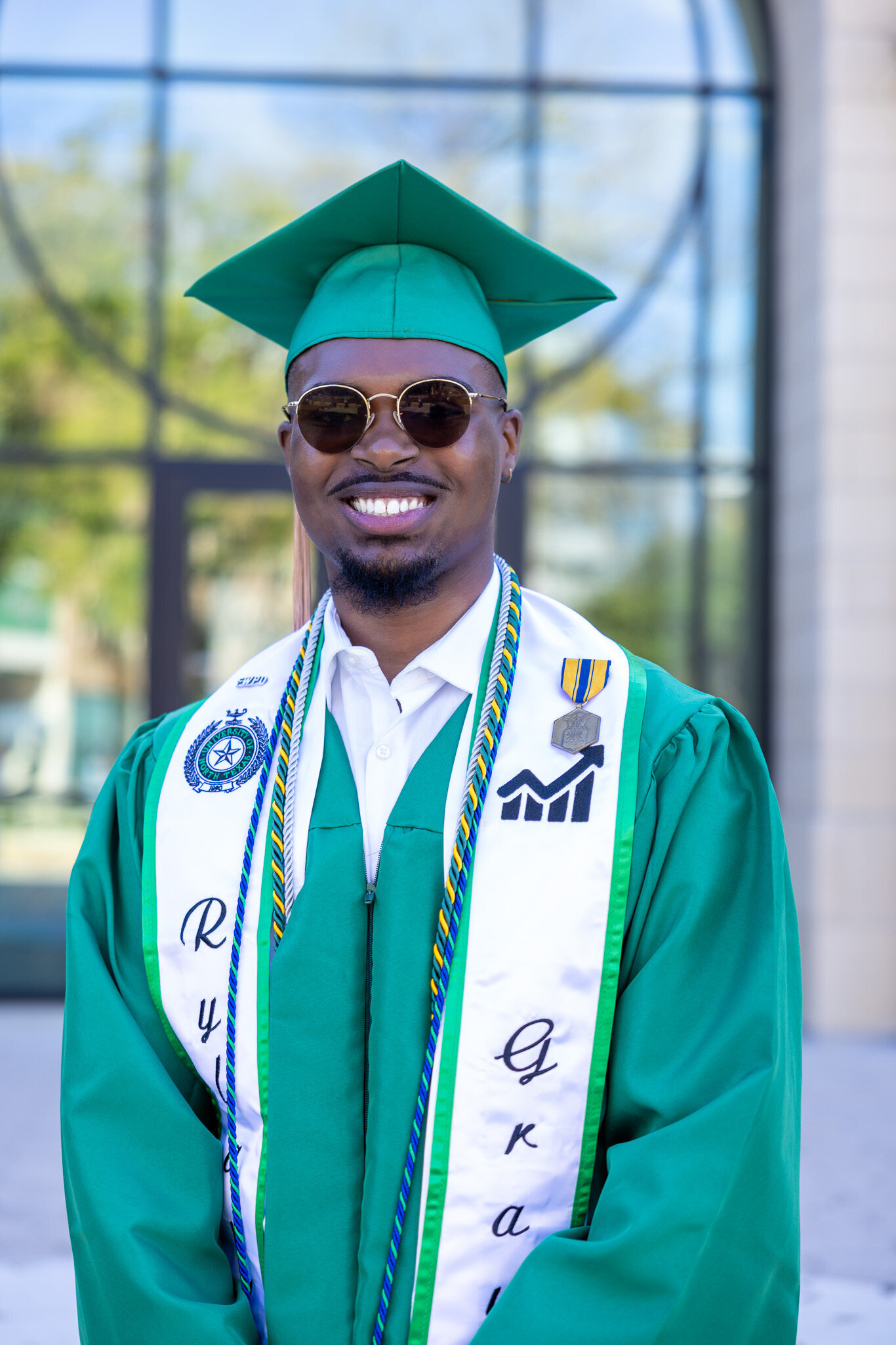 a college grad smiling in a green cap and gown