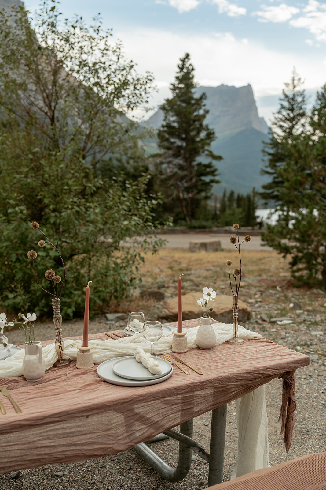 Close-up of an outdoor elopement table styled with blush-toned linens, ceramic plates, and simple floral accents in the Montana mountains.