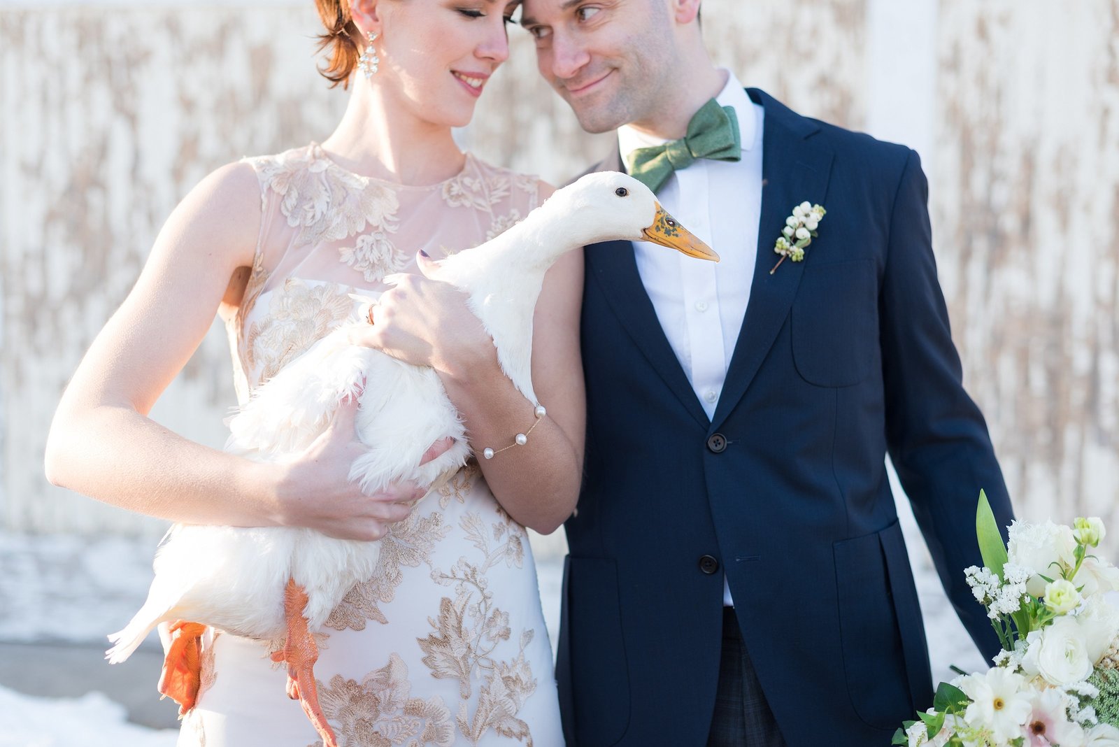 Couple looking at each other while Bride holds a duck in front of rustic barn door photo