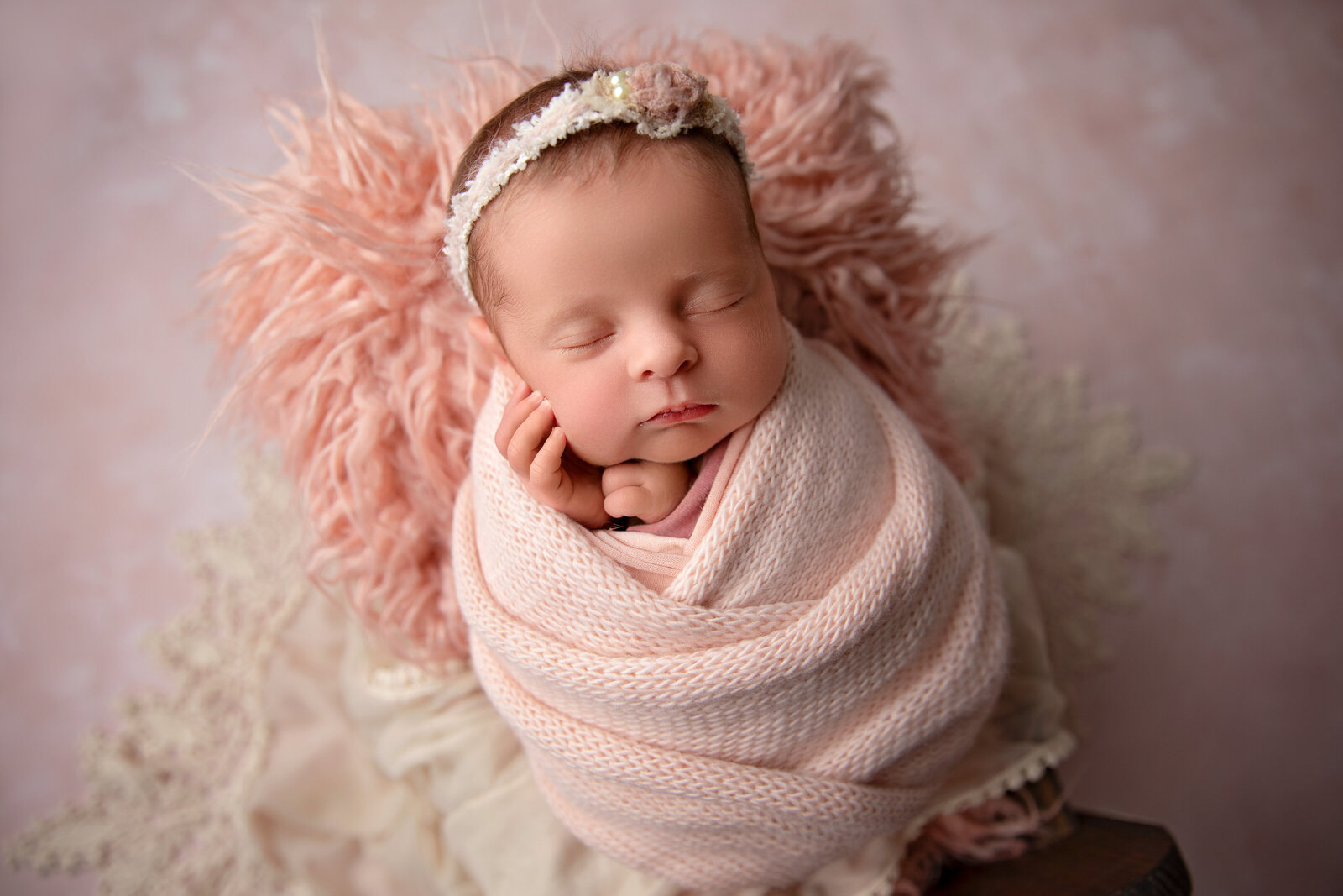 A sweet newborn baby sleeps peacefully in a small crib adorned with soft pink pastel blankets, her delicate fingers gently showcased. Captured at Little Legacies Studio in Phoenix, Arizona, this image celebrates the precious details of your baby's earliest days.