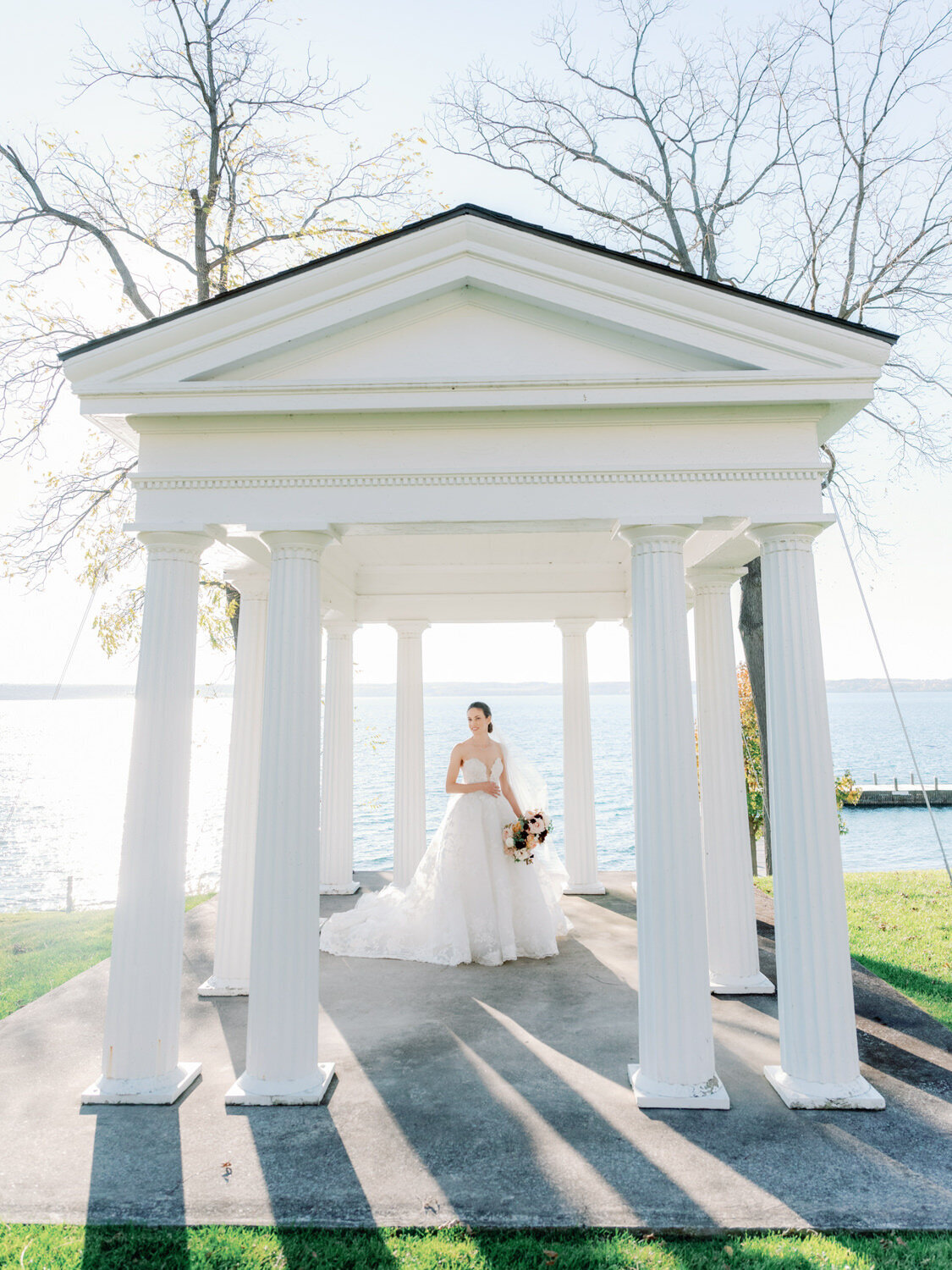 Bride stands in a white columned pergola with the sun cascading in on her.