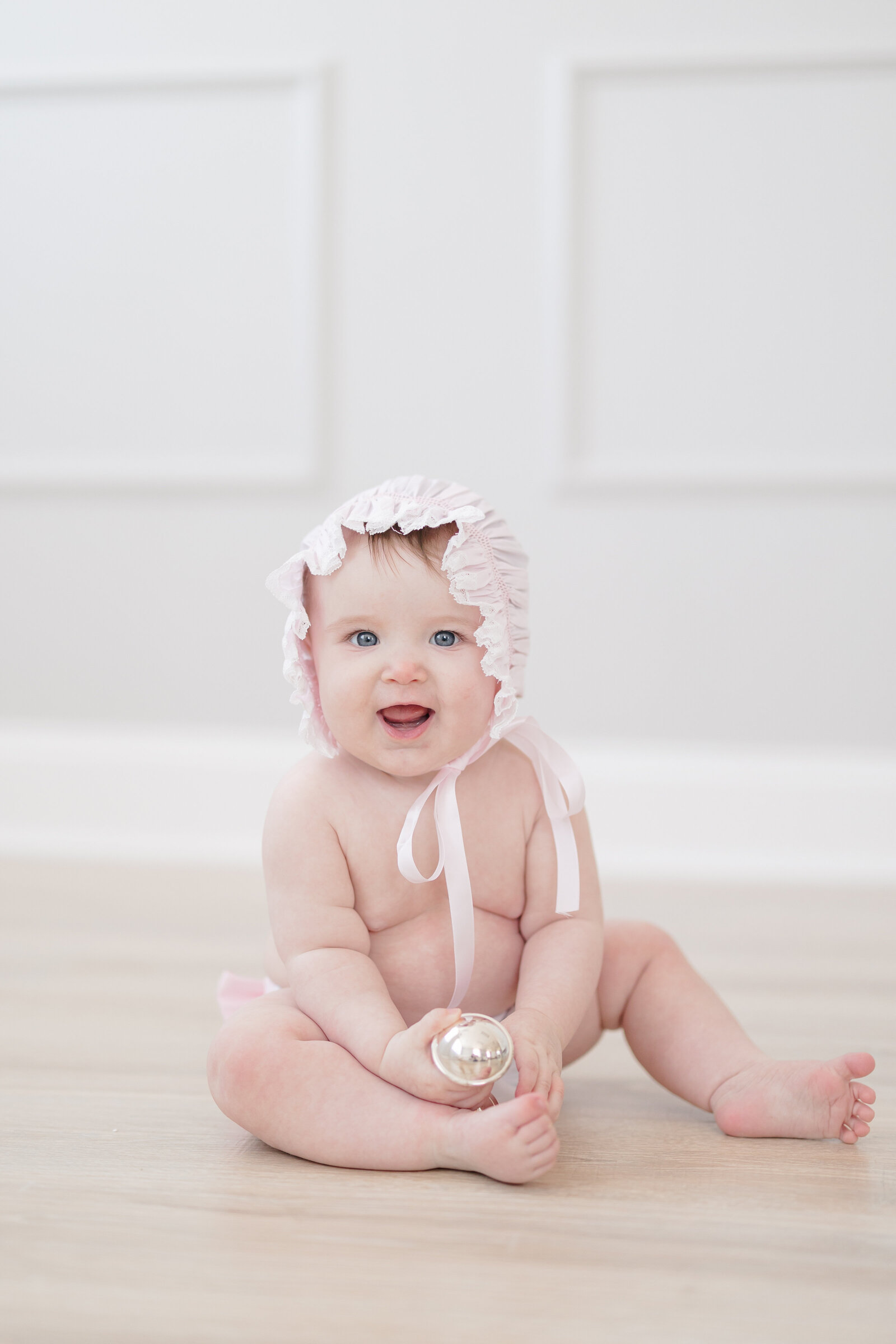Baby girl sitting on the floor wearing a smocked pink bonnet and diaper cover