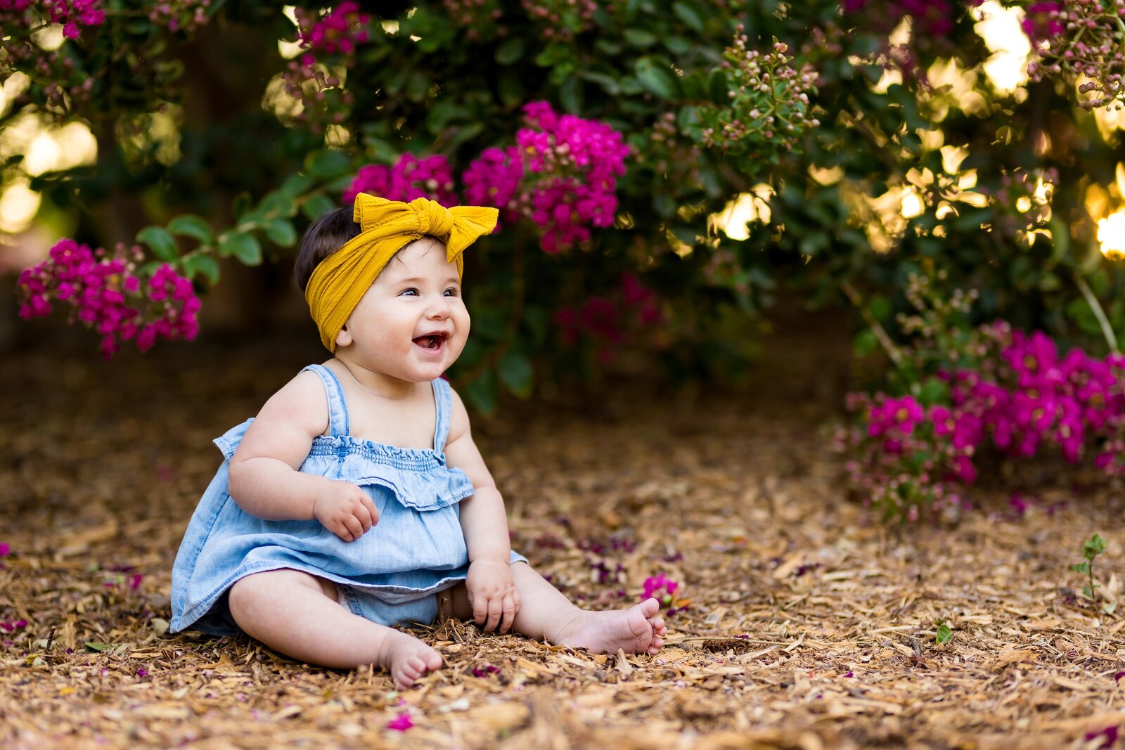baby girl smiling near flower bush