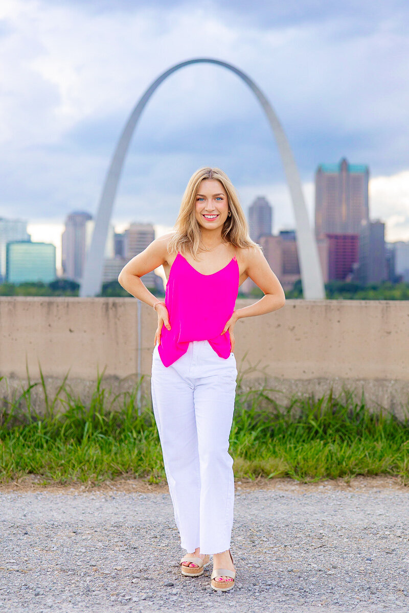 senior perfectly framed in st. louis arch with st. louis skyline behind her