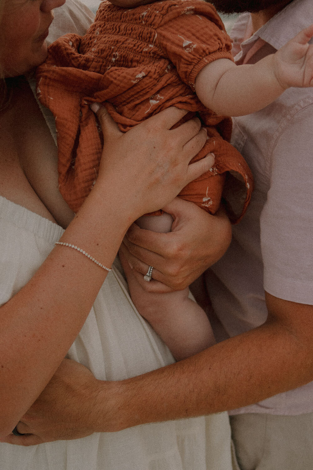 Close-up of baby in orange outfit held by parents