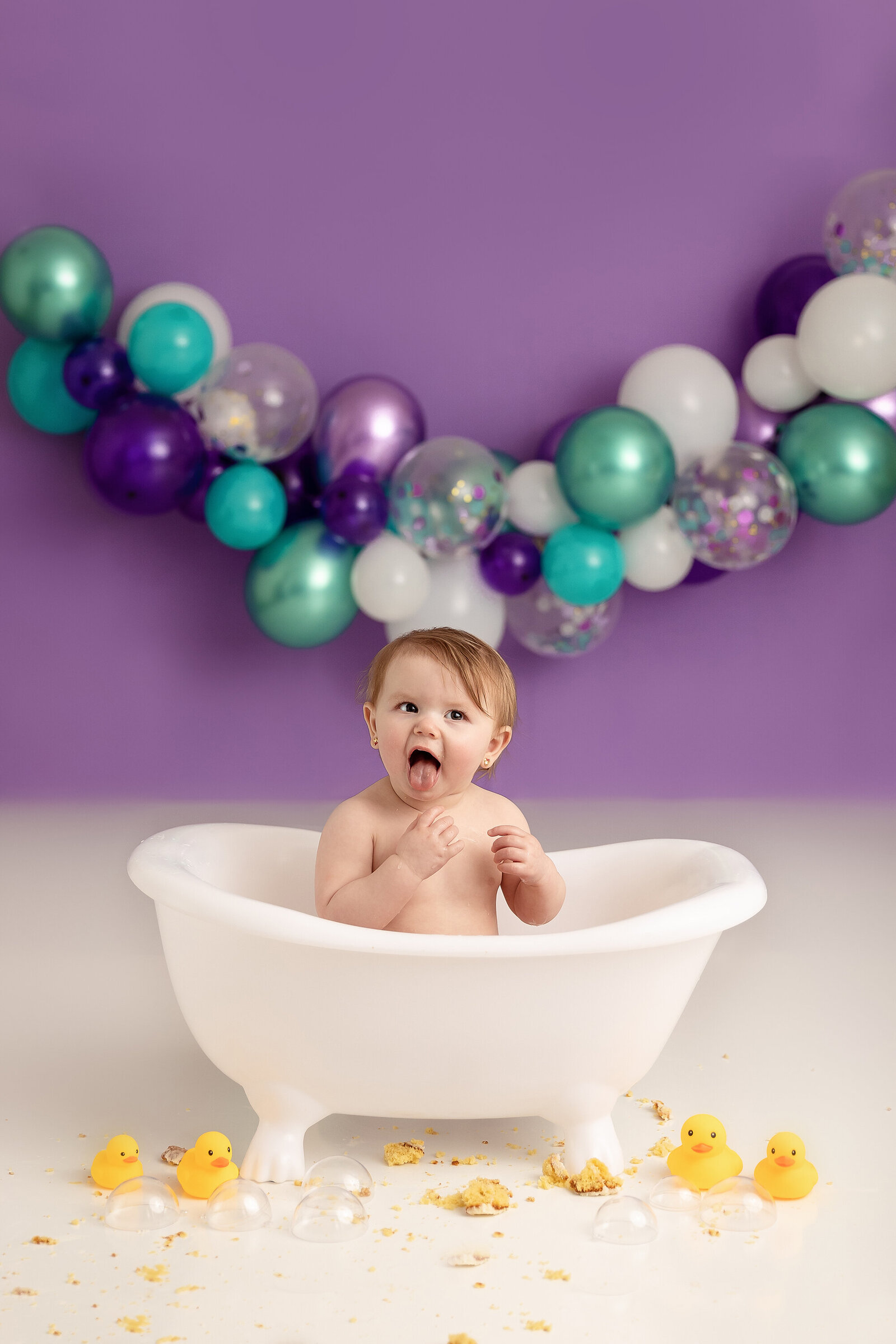 baby girl with tongue out  in tub with rubber ducks in studio by Milestone Photographer New Philadelphia