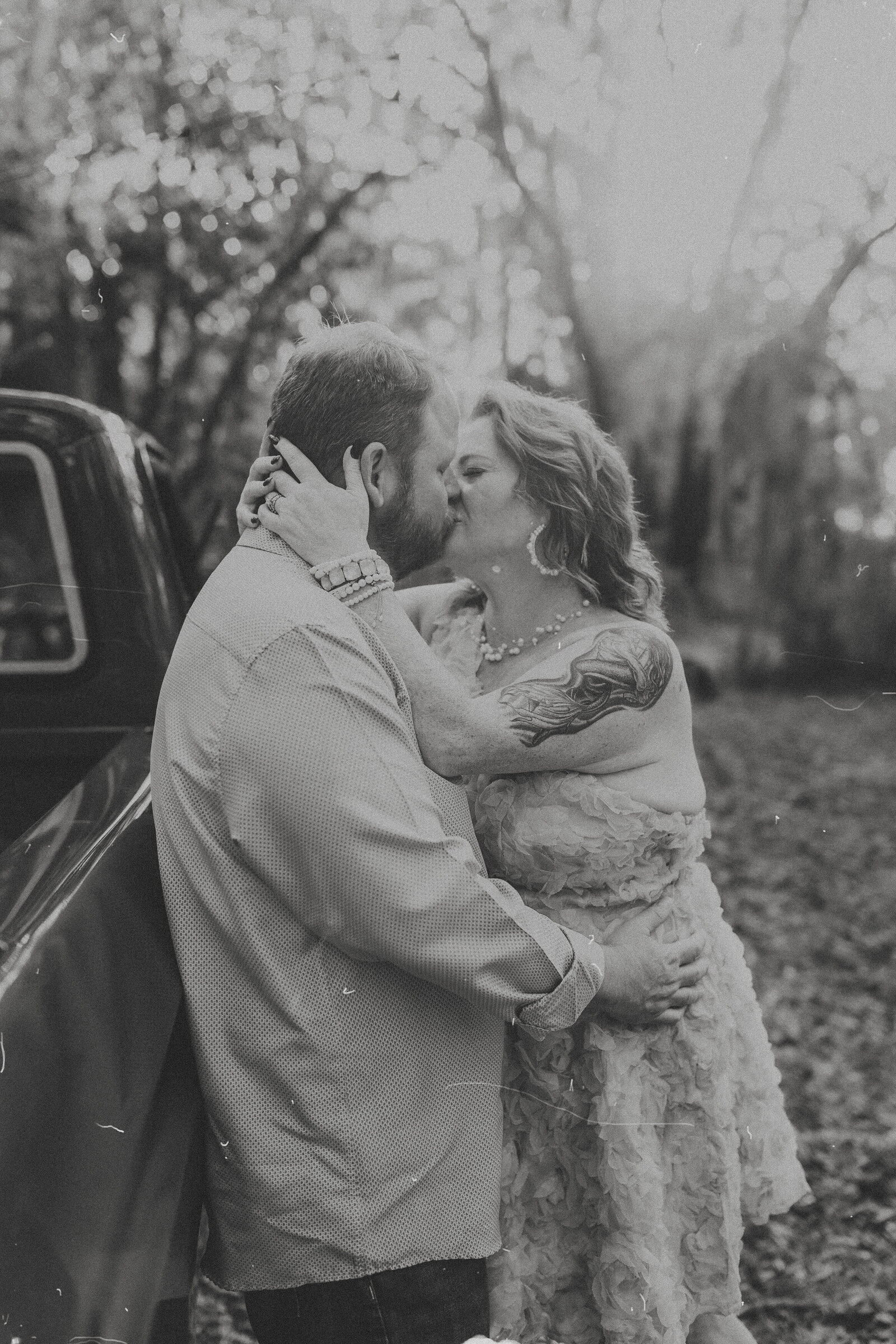 Black and white of couple in passionate kiss leaning against vintage truck