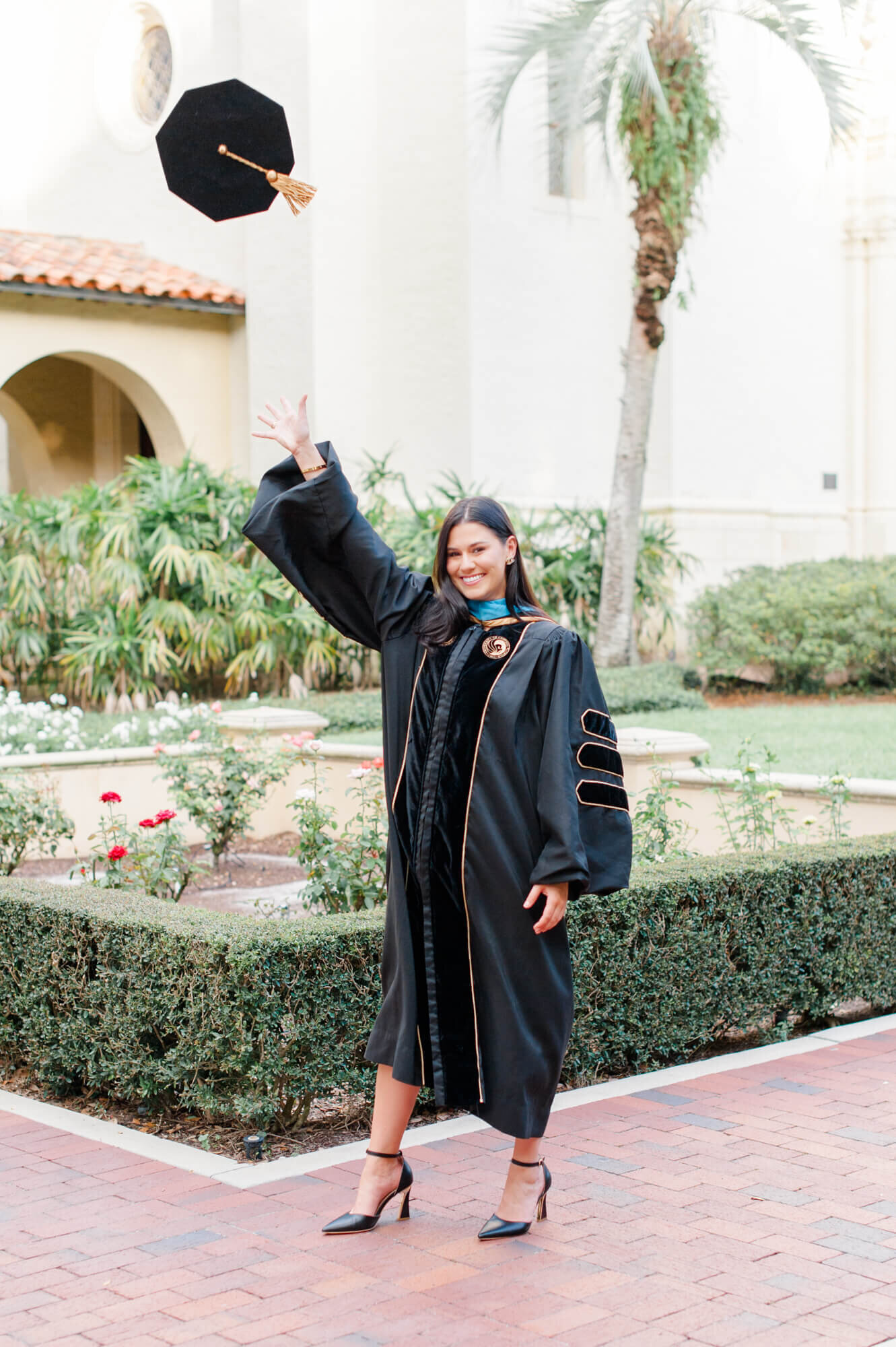 Senior girl standing in her gown throwing her cap at Rollins College during her senior photographer session