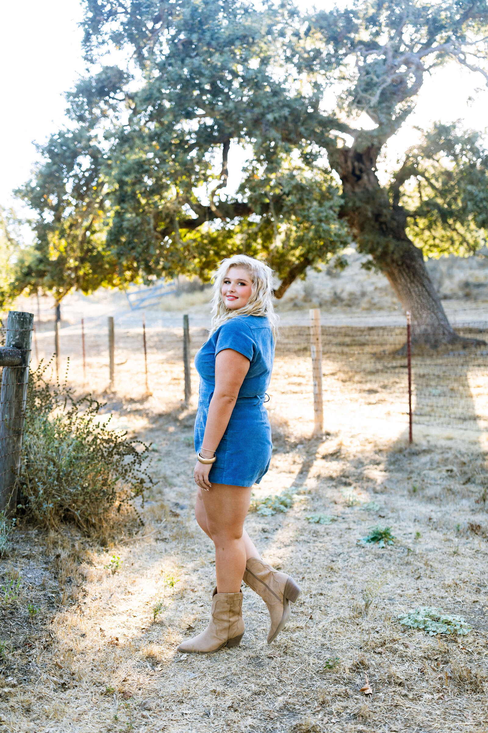 blonde girl wearing blue jean romper posing in a ranch