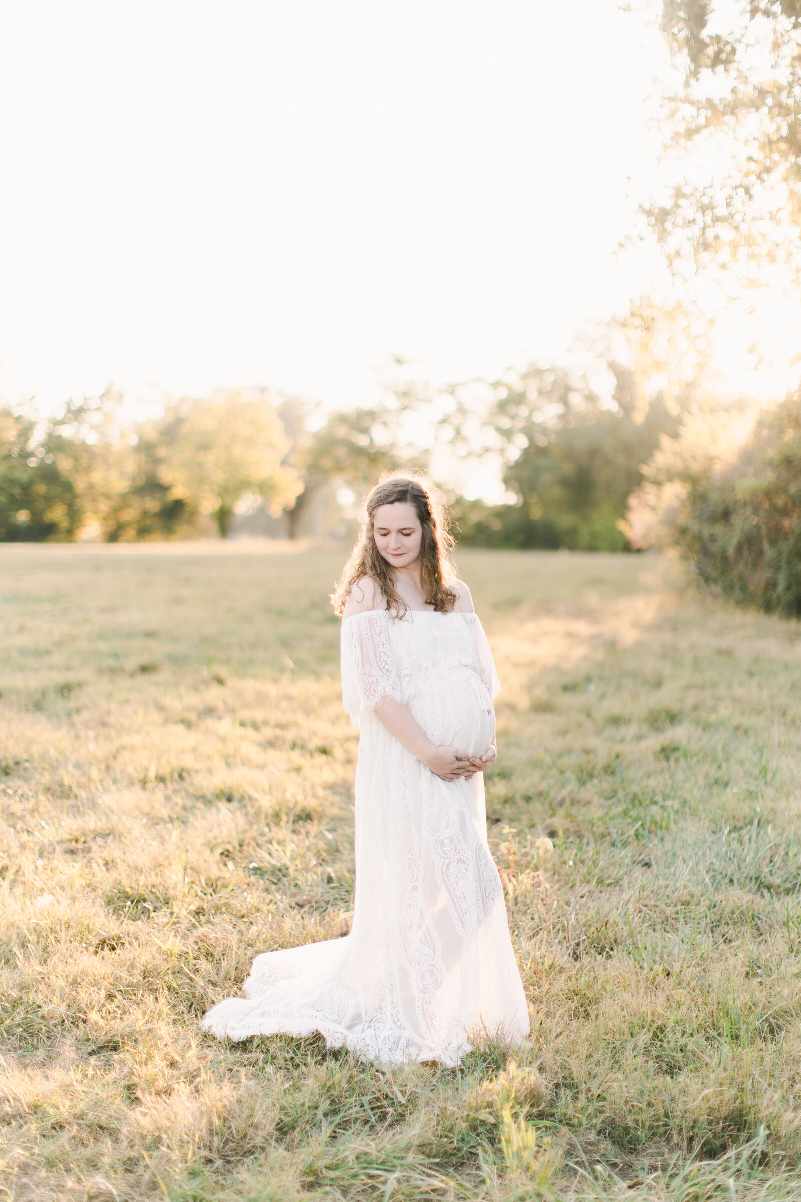 Mom in white dress in her field maternity photo shoot.