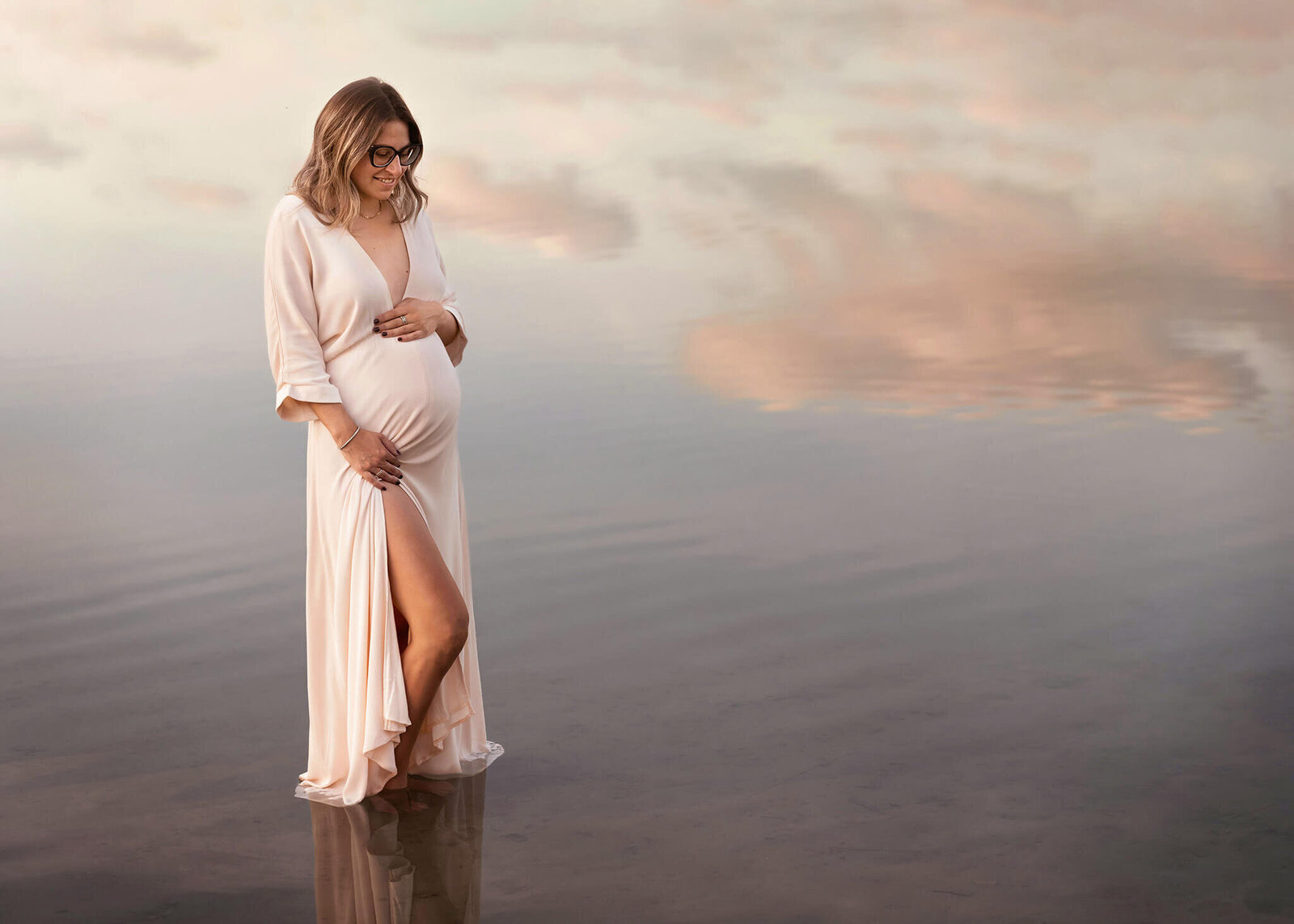 Pregnant mother stands in lake with clouds reflecting in water