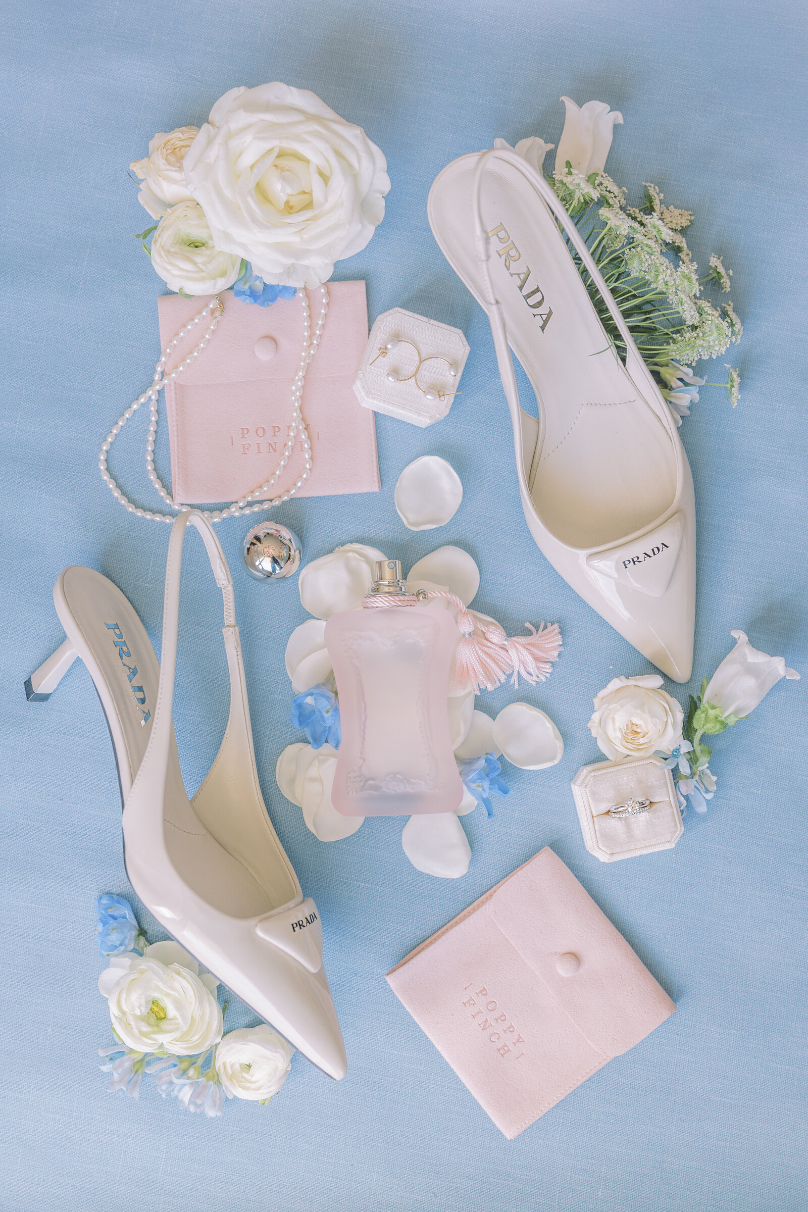 Prada shoes, perfume and jewelry flat lay for wedding in Hawaii with blue backdrop