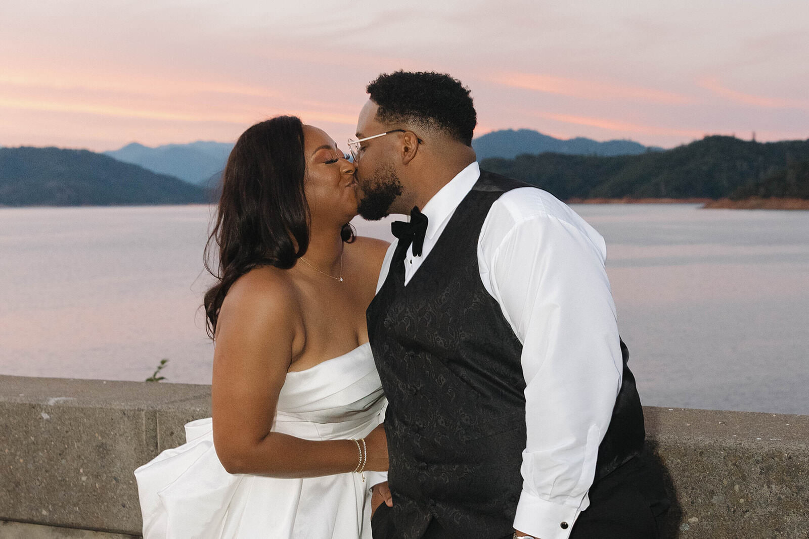 Bride and groom kissing by the lake at sunset