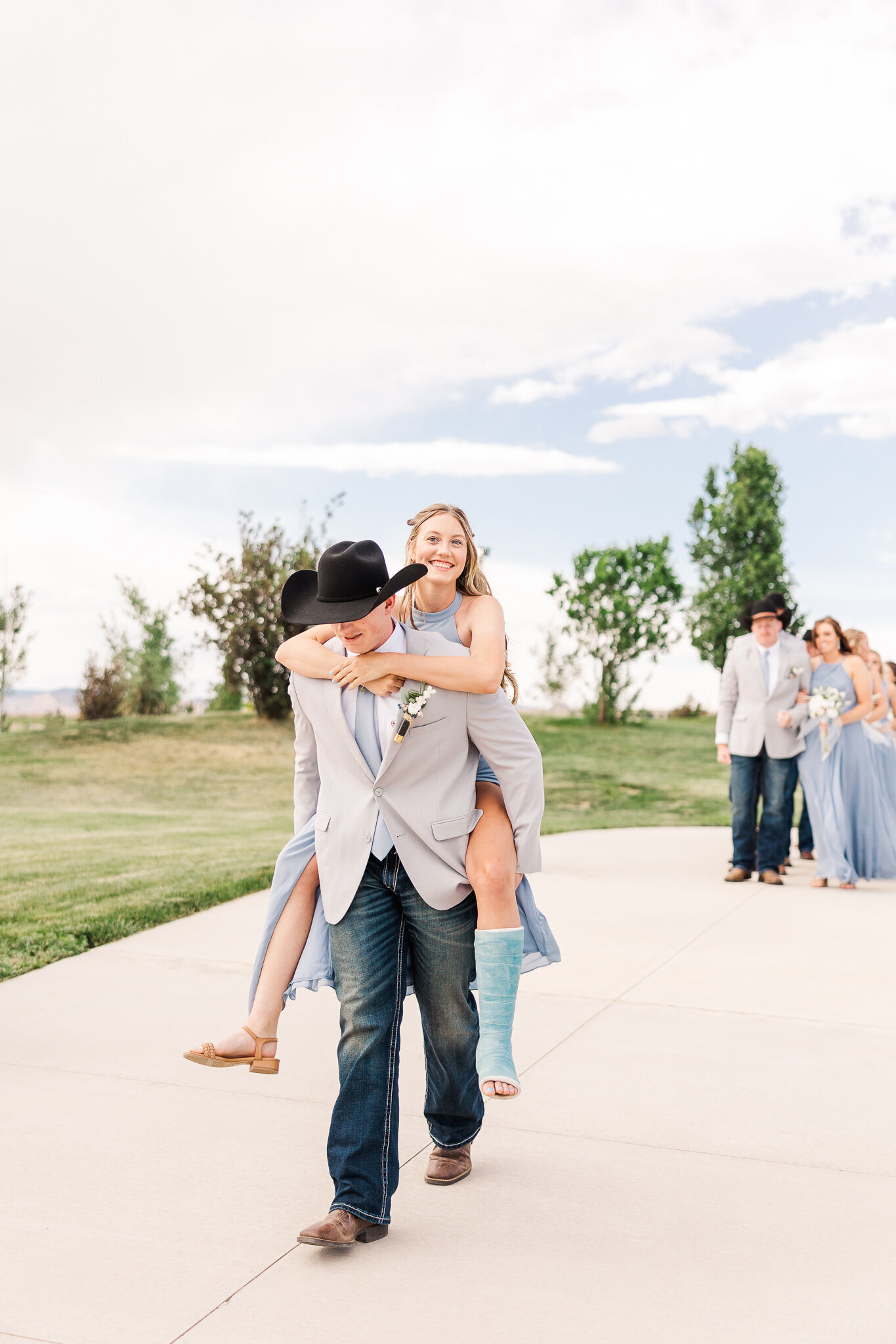 Groomsman giving bridesmaid a piggyback ride down the aisle after she broke her foot at a fun and memorable Loma wedding.