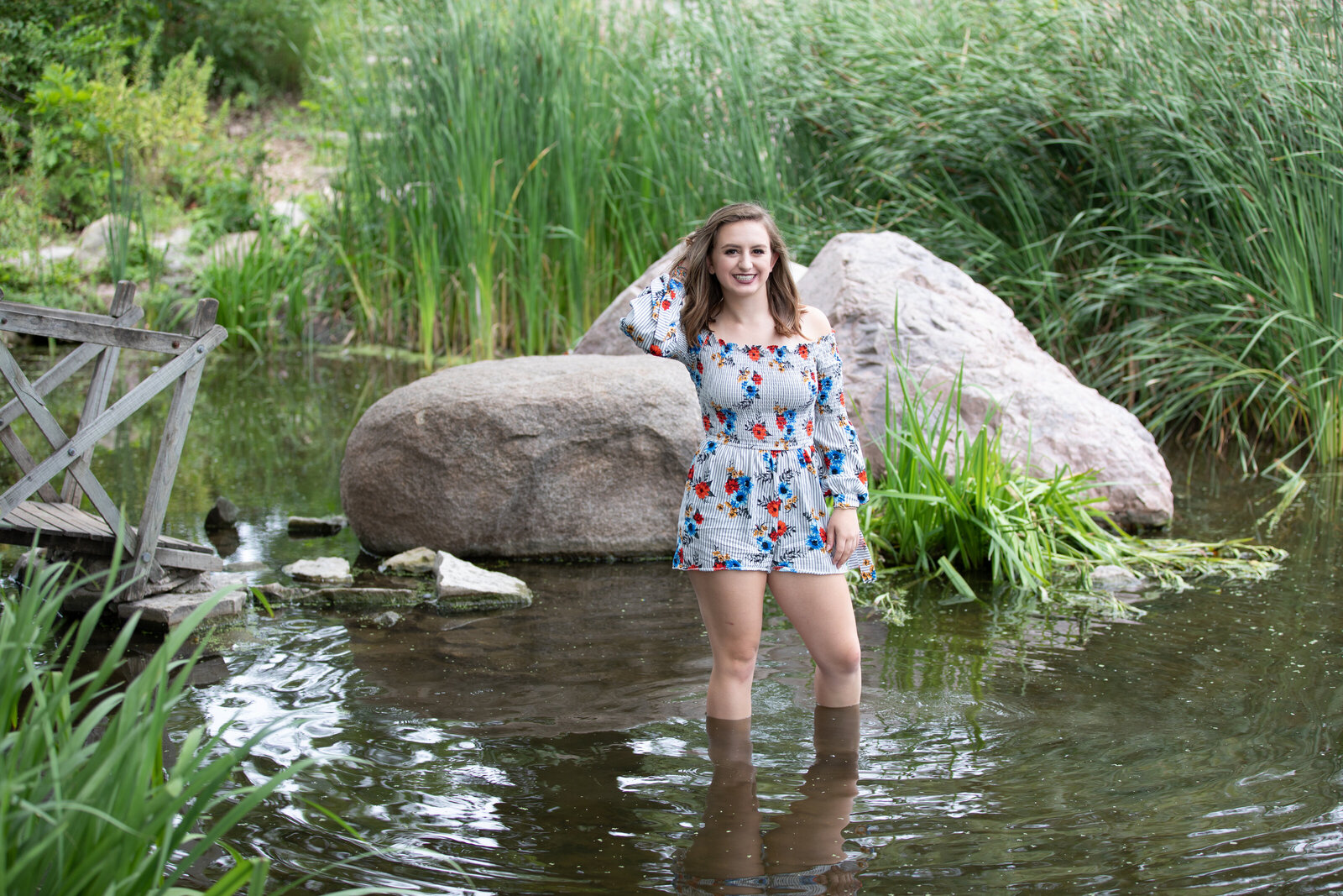 Senior stands in water in front of a rock
