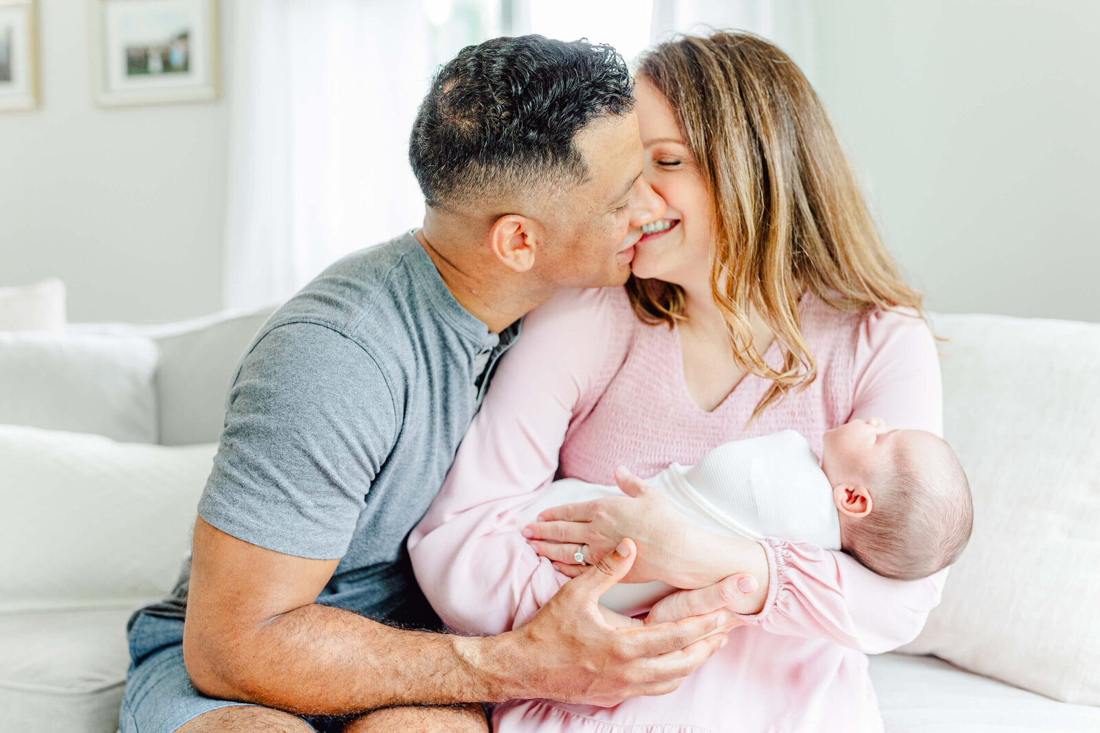 Mom and dad giggle as they lean in for a kiss while mom holds the newborn