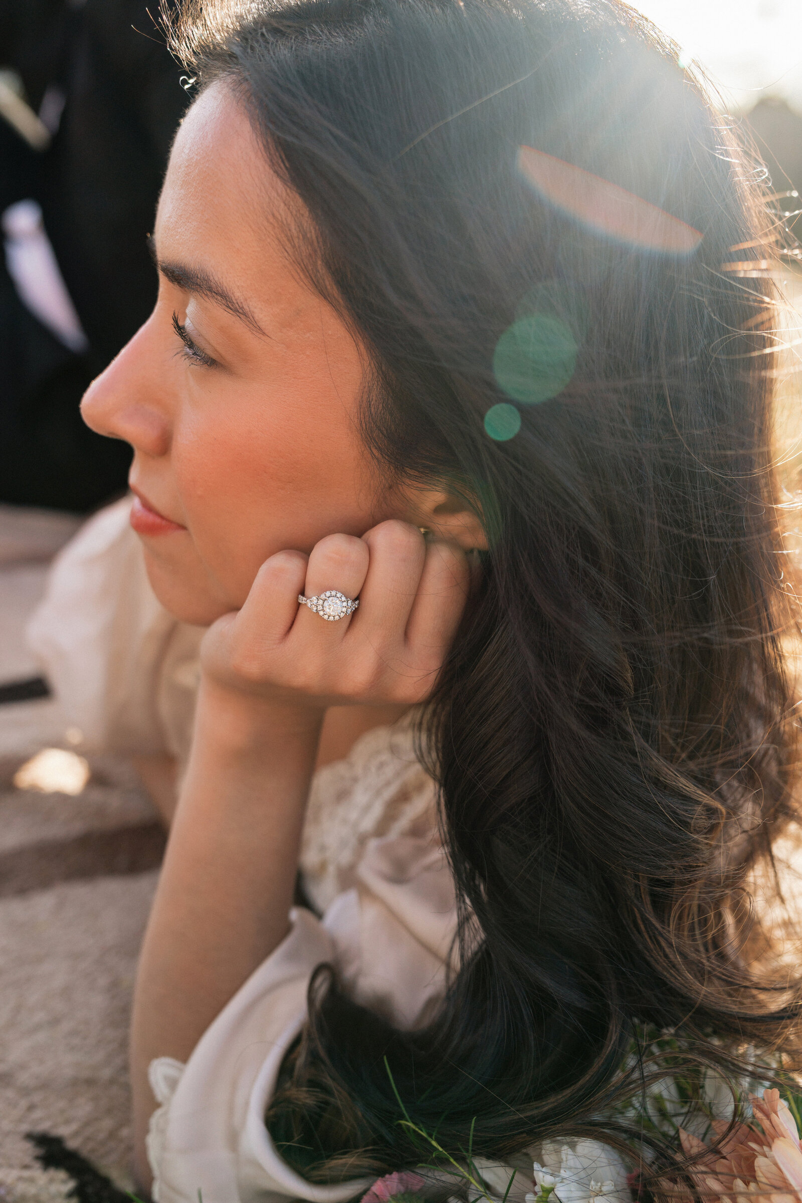 Close-up of a bride resting her chin on her hand, showcasing an oval diamond engagement ring with sunlight flares, captured during an elopement at Bear Mountain in Sedona, Arizona.