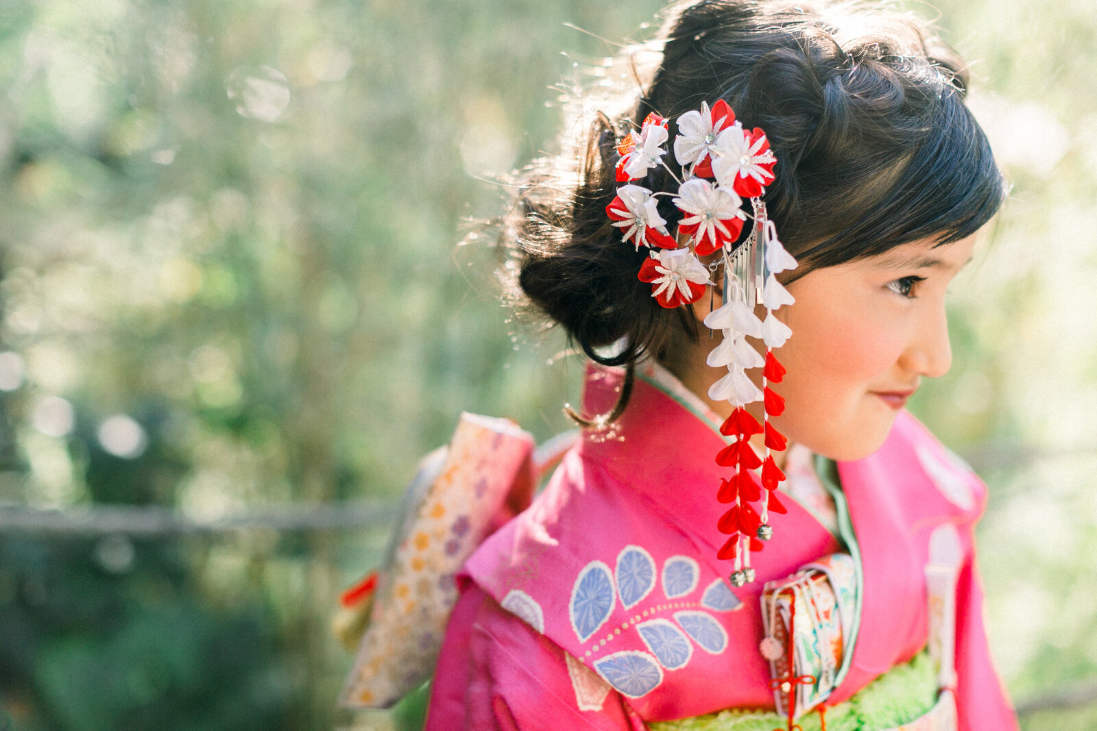 Close-up of girl wearing pink kimono with red tsumami kanzashi hair ornament outdoors | 七五三 女の子 ピンク着物 つまみ細工髪飾り 屋外ポートレート