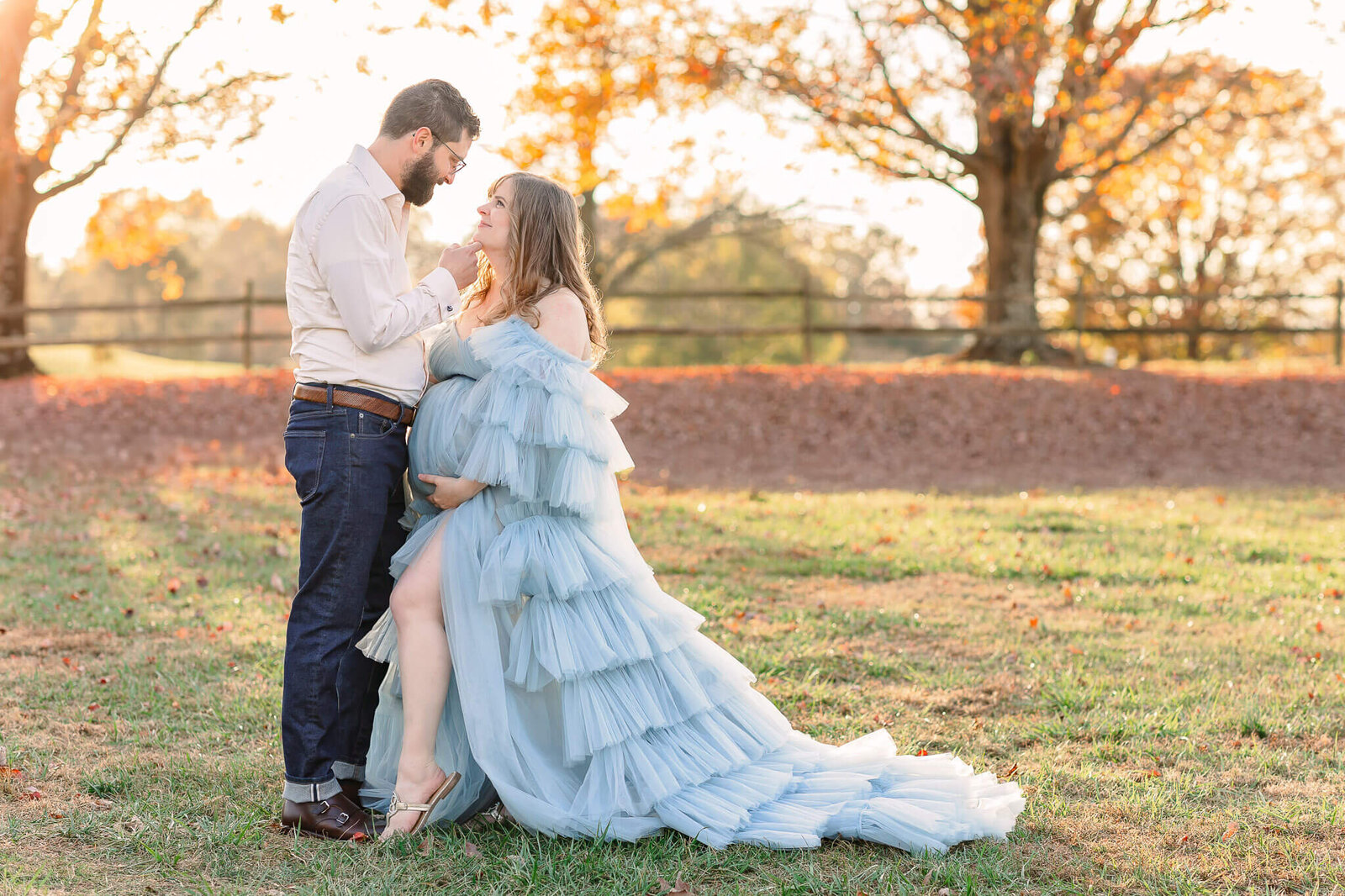 A couple that is expecting their first baby looking lovingly at each other at a park in NOVA at sunset.