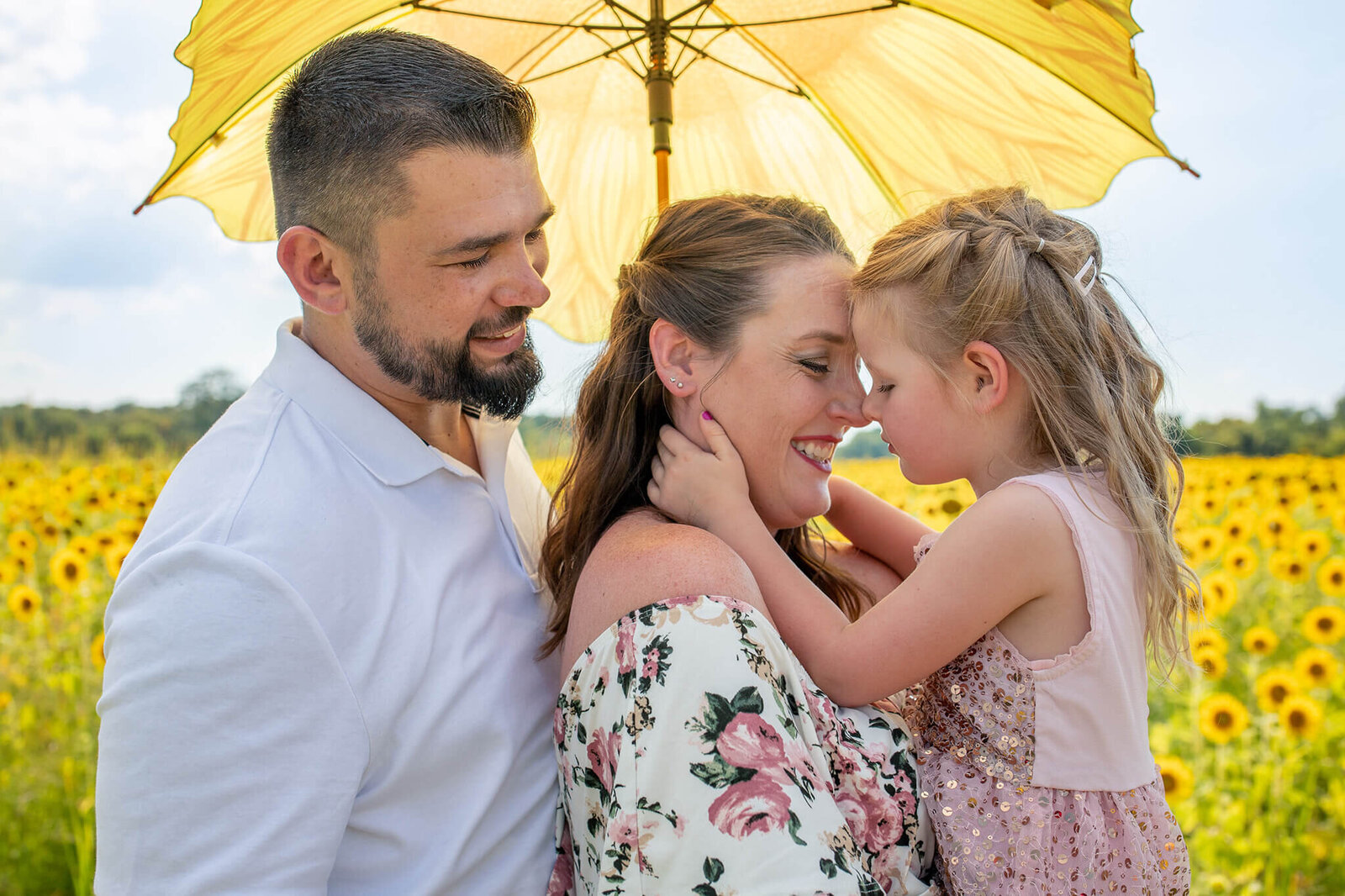 A family of three snuggling under an umbrella in a sunflower field in Northern Virginia.