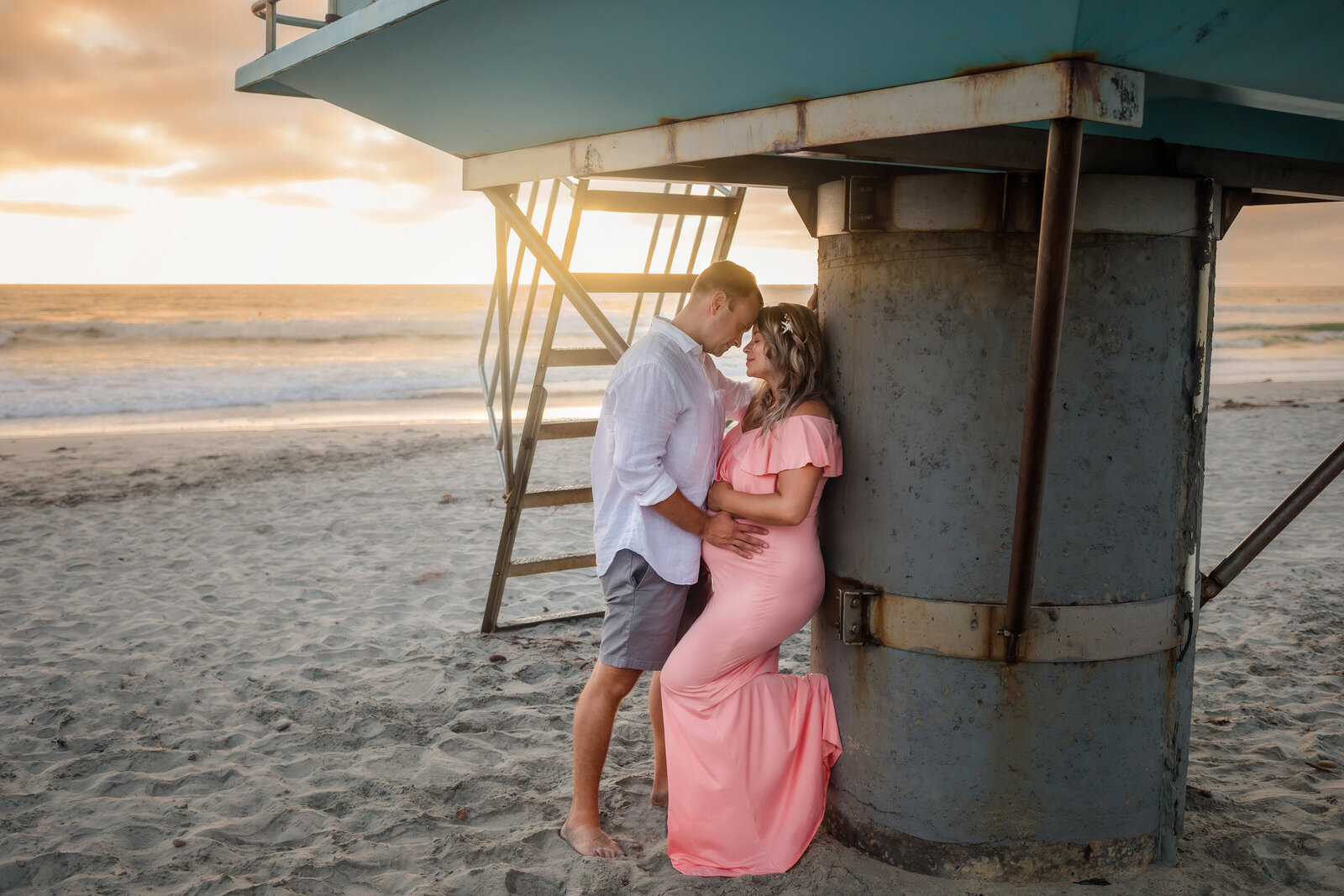 Maternity Photographer, a husband and pregnant wife recline on a lifeguard tower at the beach