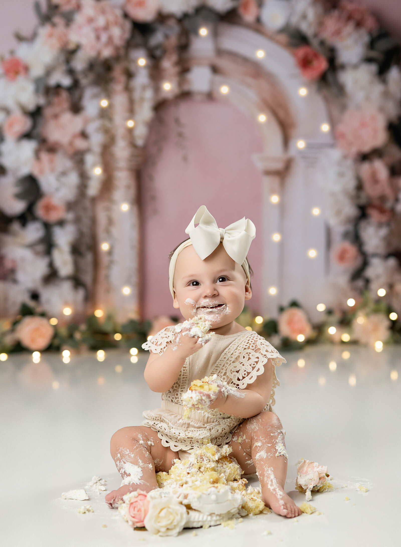 Baby girl in cream lace romper, eating birthday cake. Photographed by Atlanta photographer.