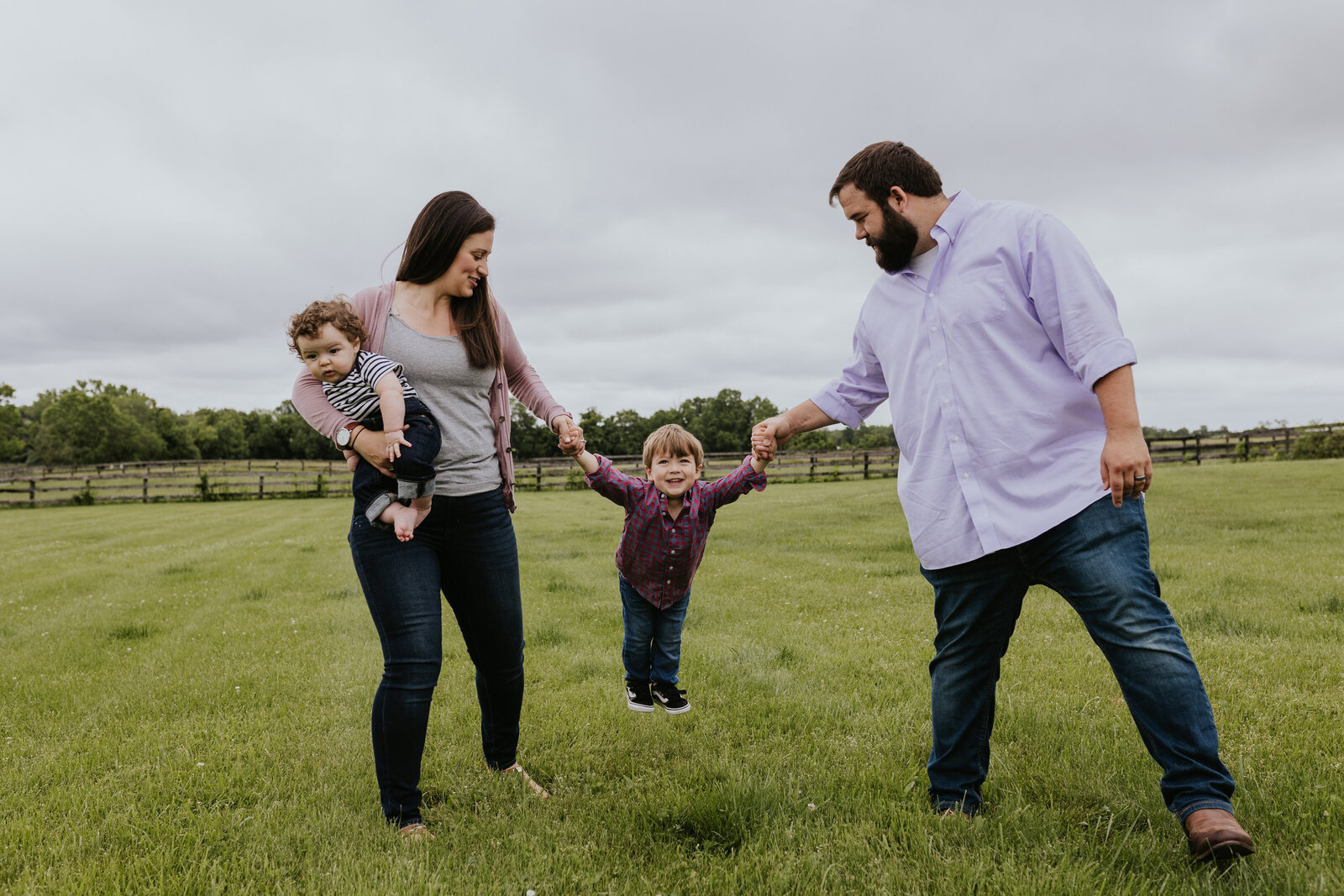 A mother and father swing their young song in a grassy field