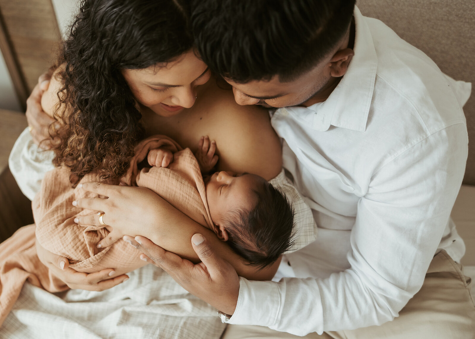 Mother and father in their bedroom at home cradling their newborn baby for their first photoshoot as a family.