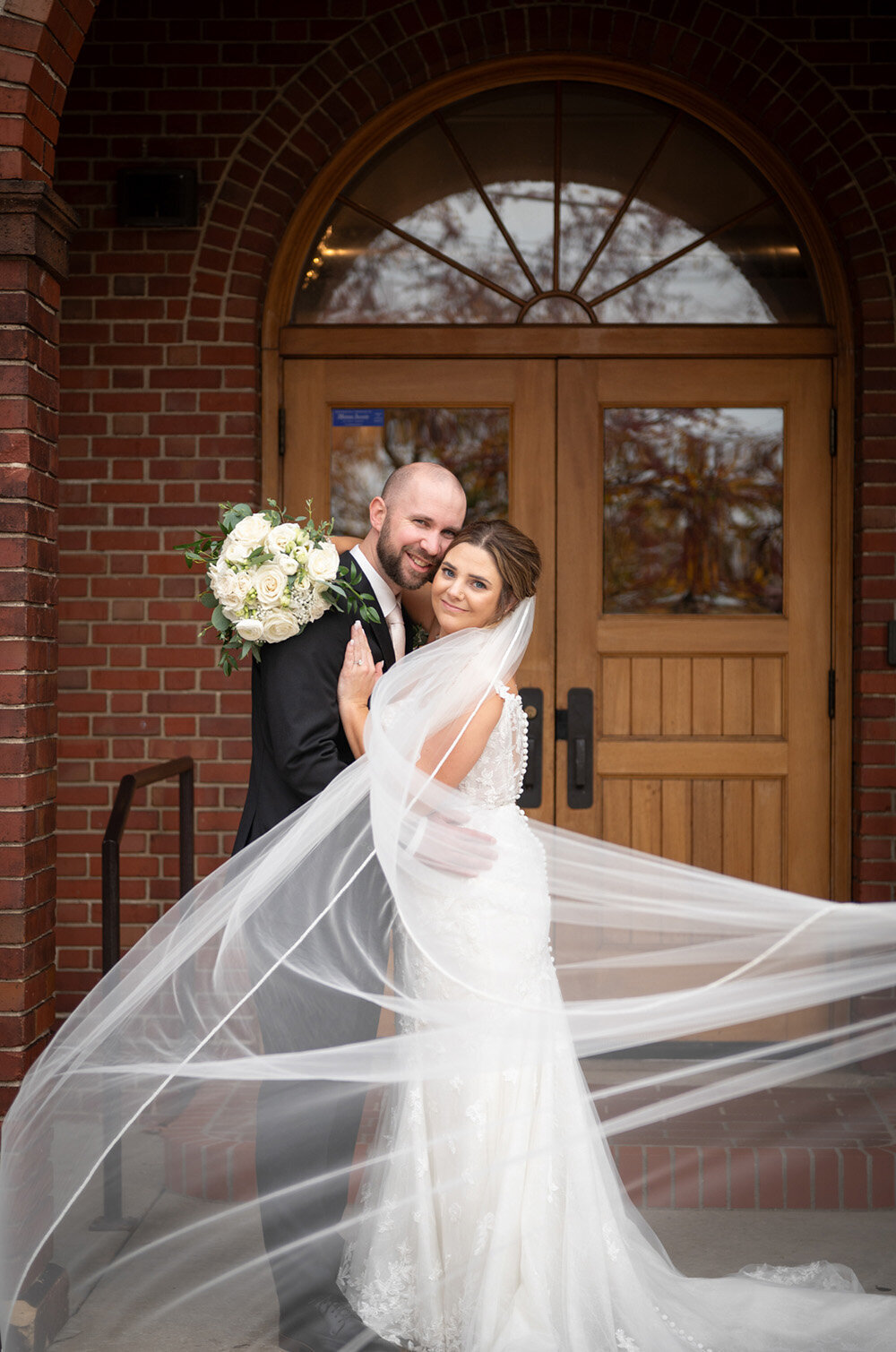 bride and groom smile together while bride's veil dances in front of them