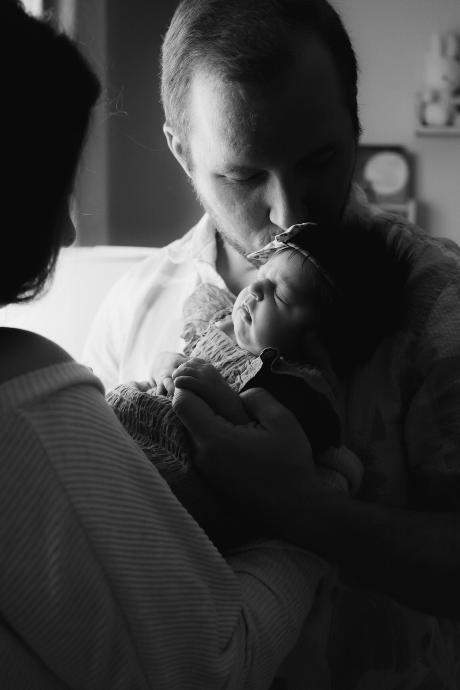 Dad kissing newborn daughter's forehead as mom holds daughter in arms.