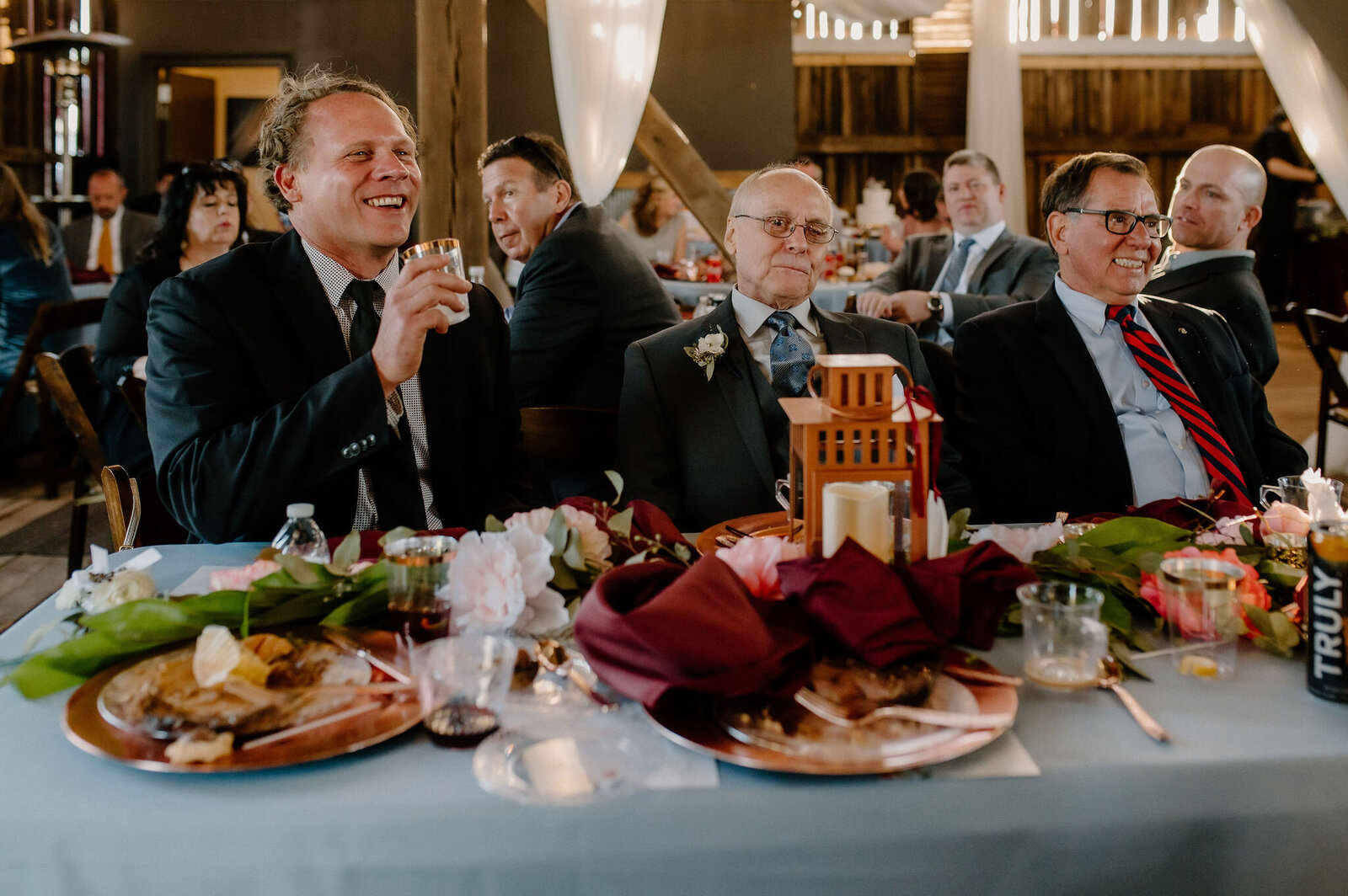 guests laughing and drinking while sitting at table during wedding reception