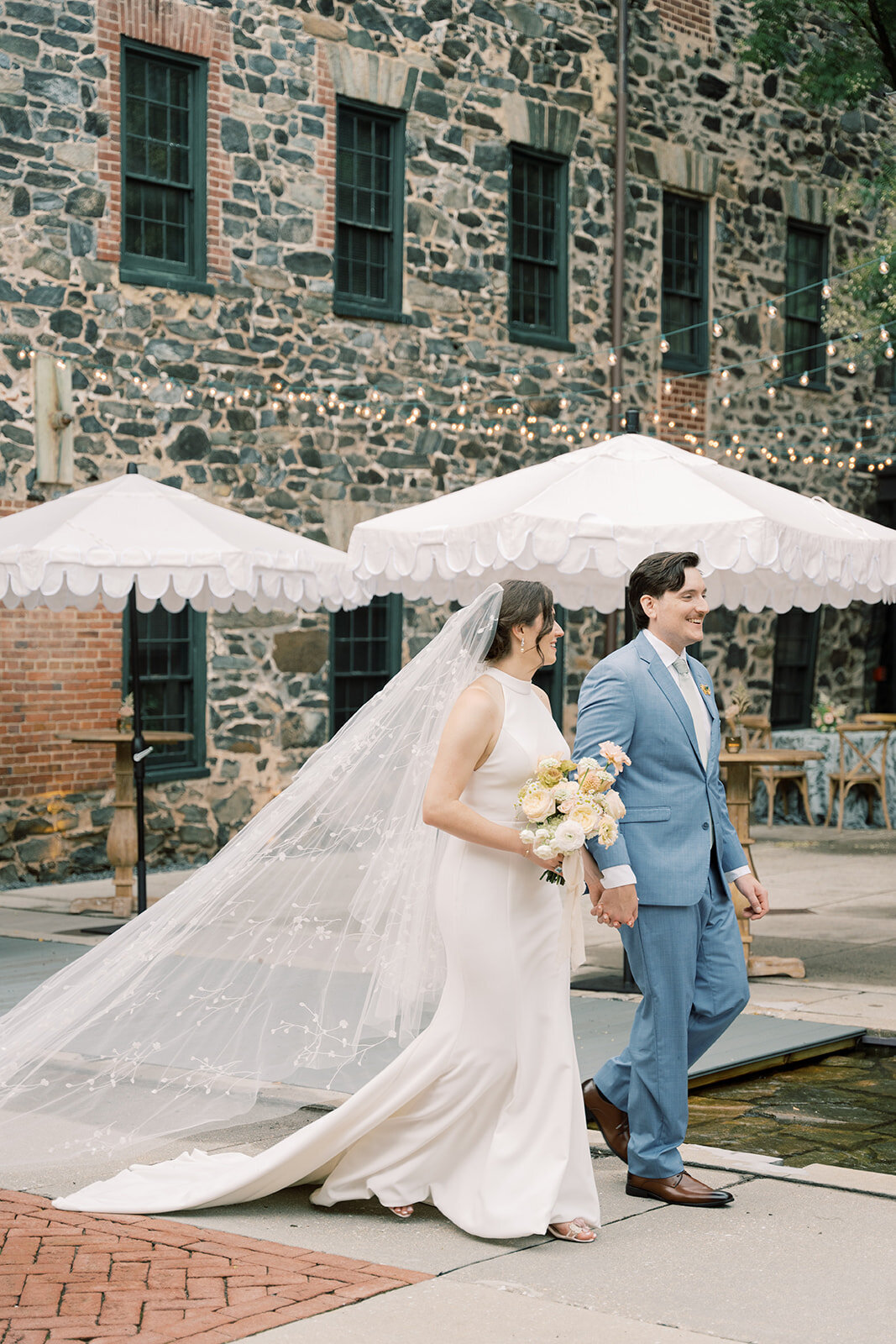 Bride and groom portrait walking outside the Washington mill dye house with white umbrellas in the background.