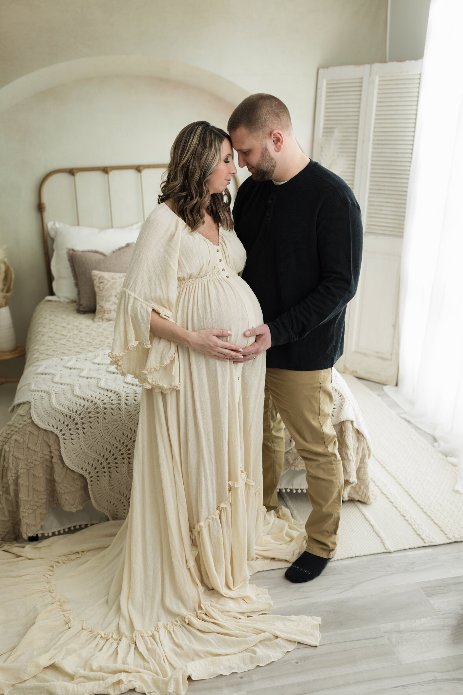 husband and pregnant wife in cream maternity gown hugging for maternity photoshoot