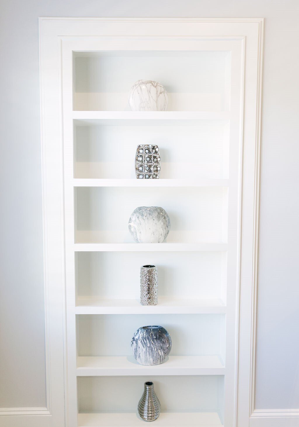 Clutter-free white bookcase organized with silver vases