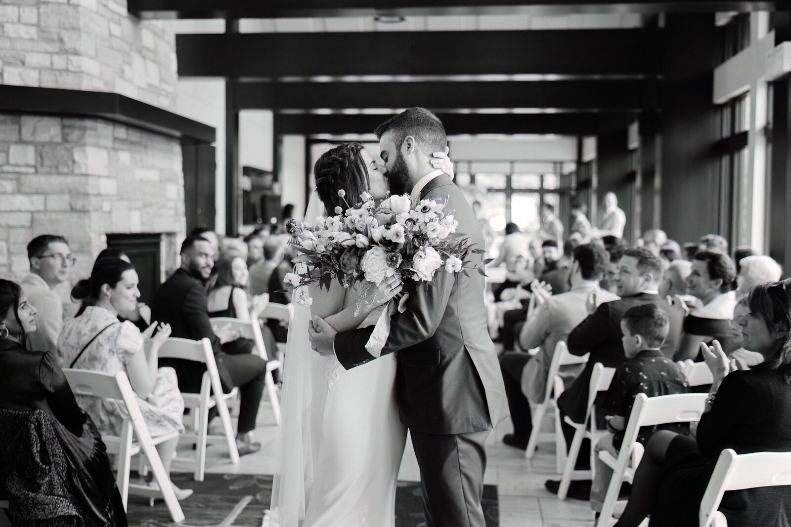A black and white photo of the bride and groom sharing a kiss after the wedding