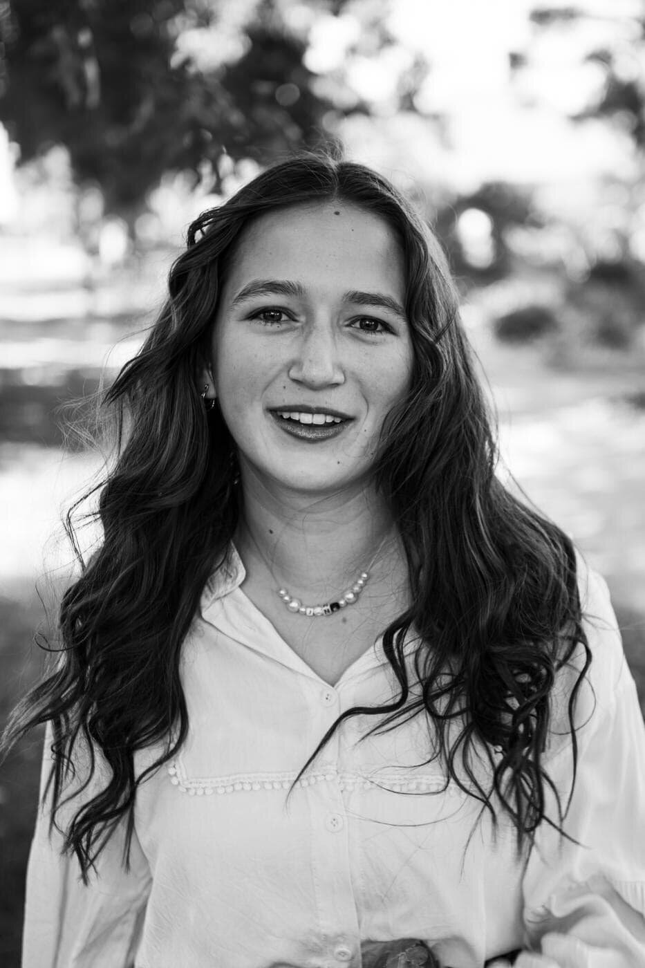 A senior girl with long dark hair looks at the camera smiling. 