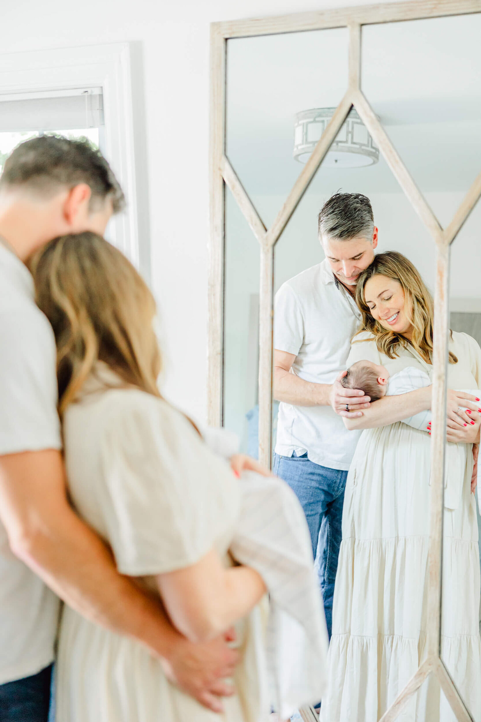 Mirror reflection showing a mom and dad standing together while mom holds the newborn