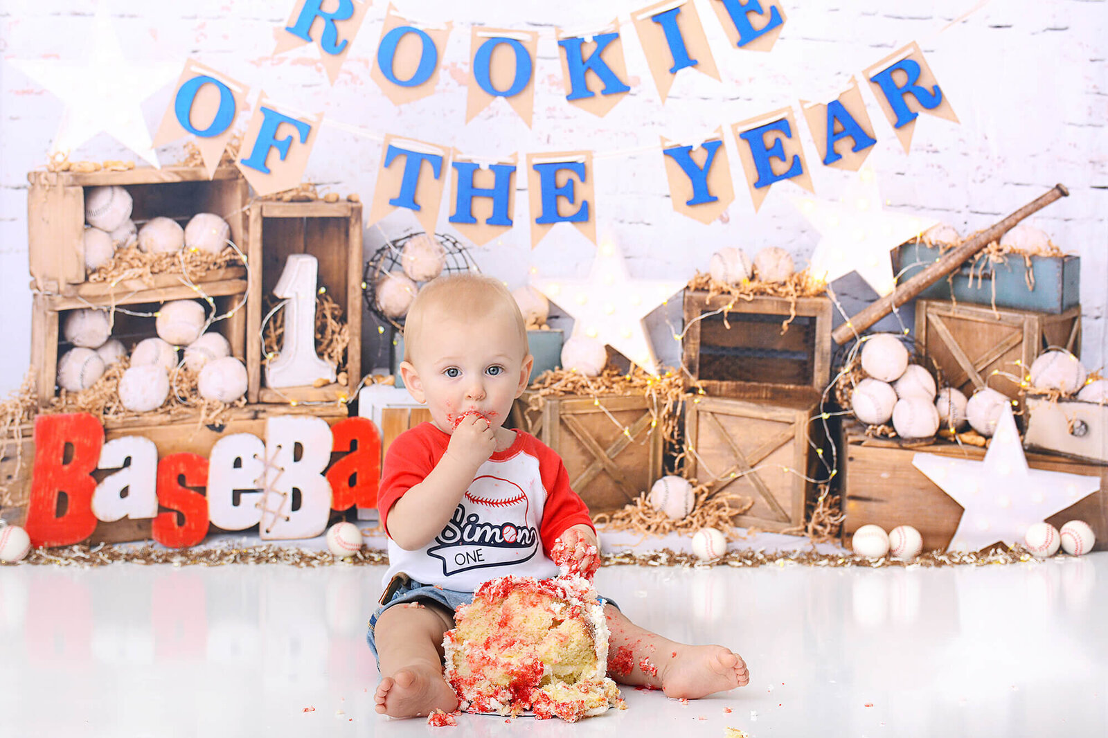 boy eats his birthday cake  at his first birthday photoshoot in houston with a baseball rookie of the year theme