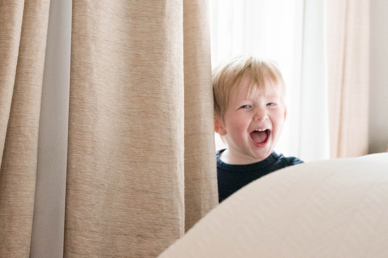 A toddler playing peek a bo behind a curtain