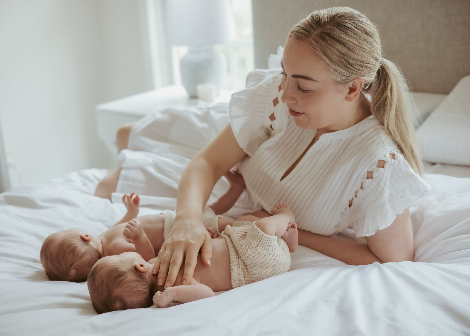 An intimate in-home photography experience for a mum wearing white lying on the bed with her twin babies.