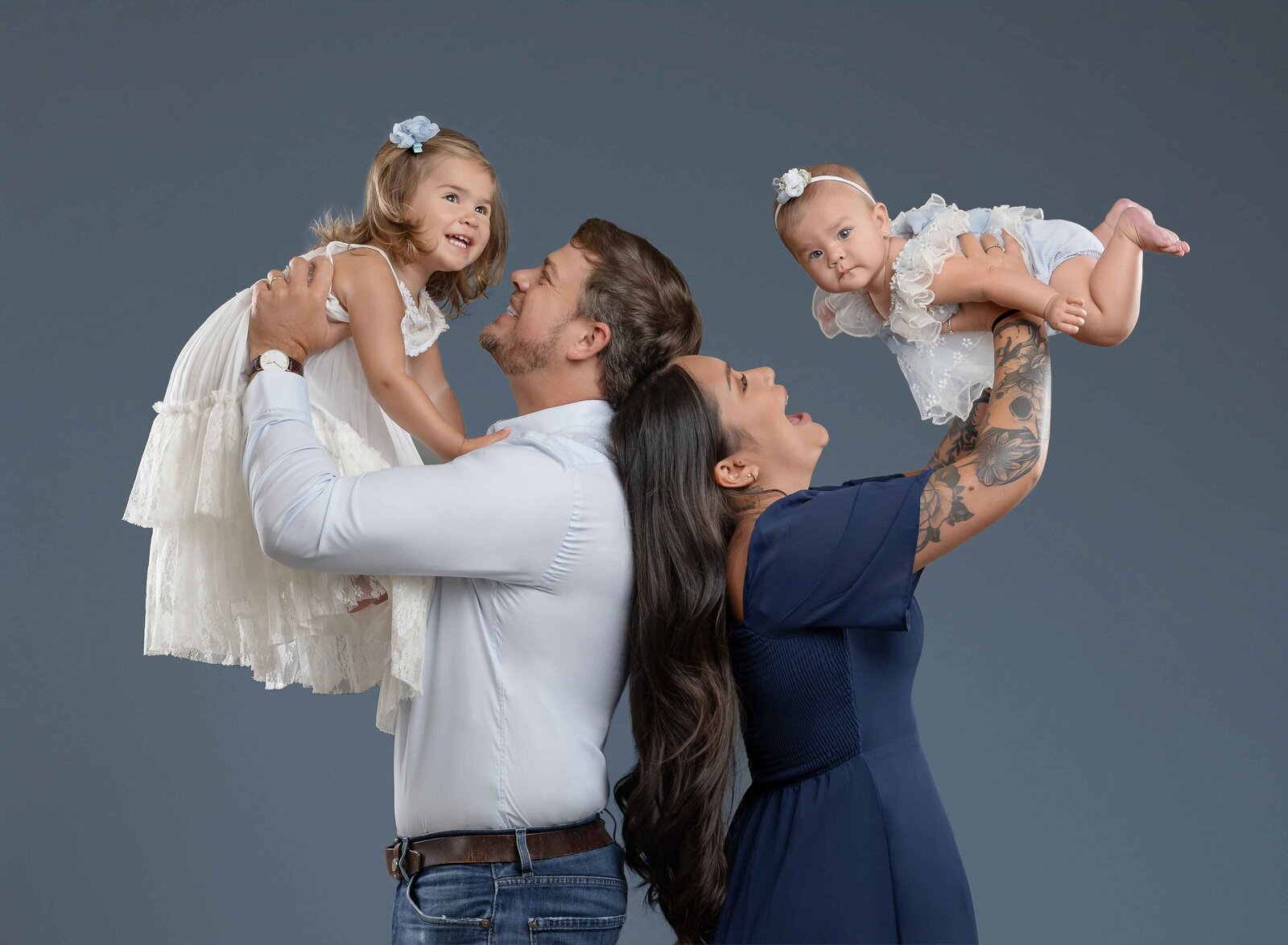 Mom and Dad tossing kids in air and laughing. family dressed in light and navy blues taking professional family portrait in Atlanta.