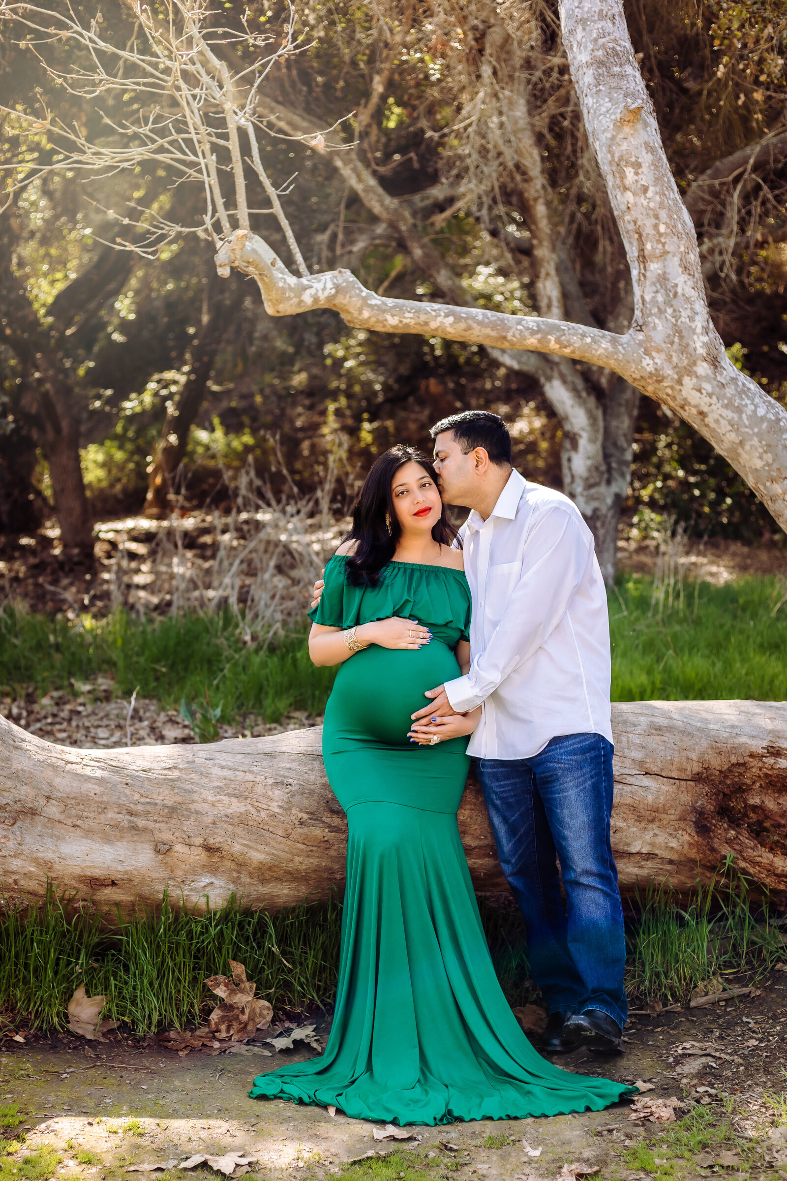 Maternity Photographer, a couoke hold each other close outside beneath trees, she is pregnant