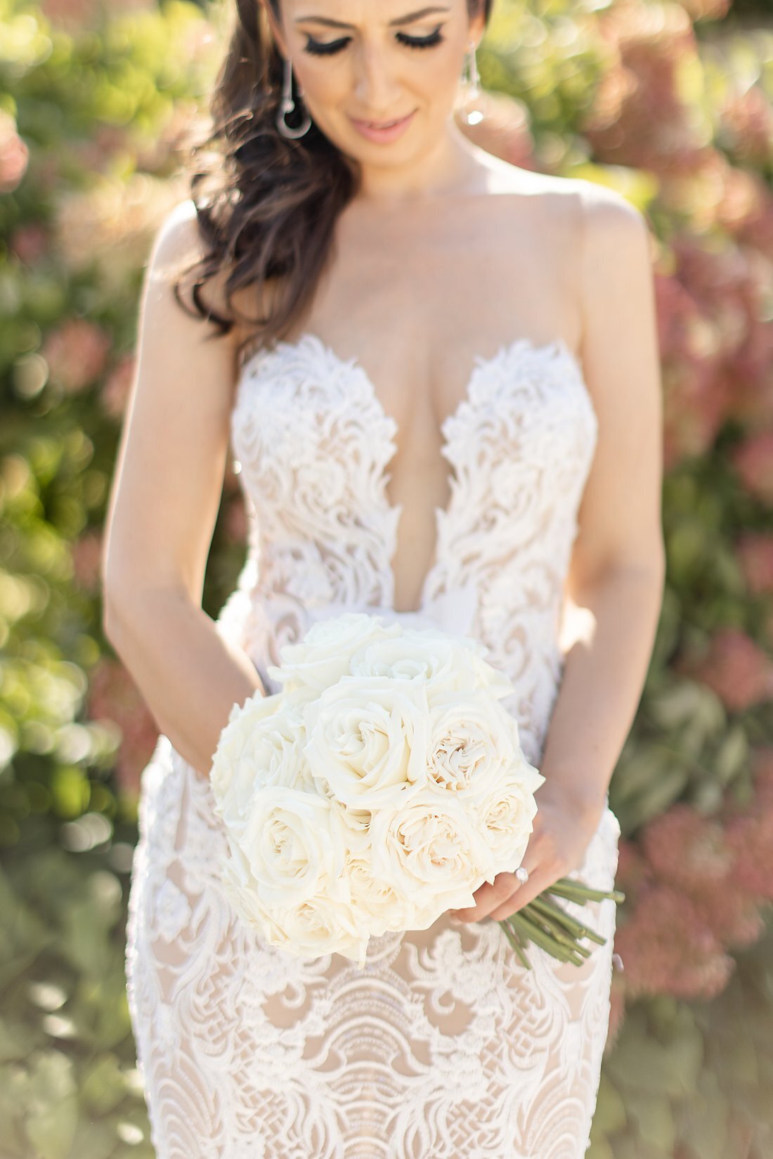 Stunning-bride-looking-down-at-her-beautiful-white-bouqet-in-her-gorgeous-low-v-wedding-dress