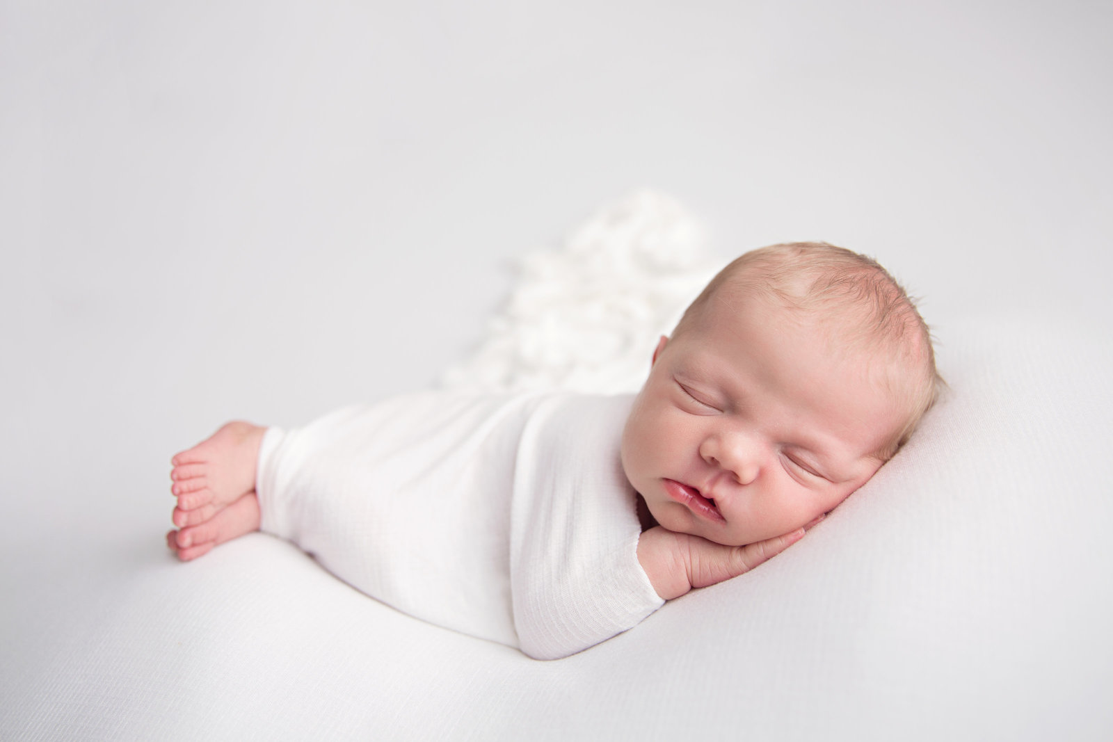 sleeping newborn baby posed on white fabric with white wrap