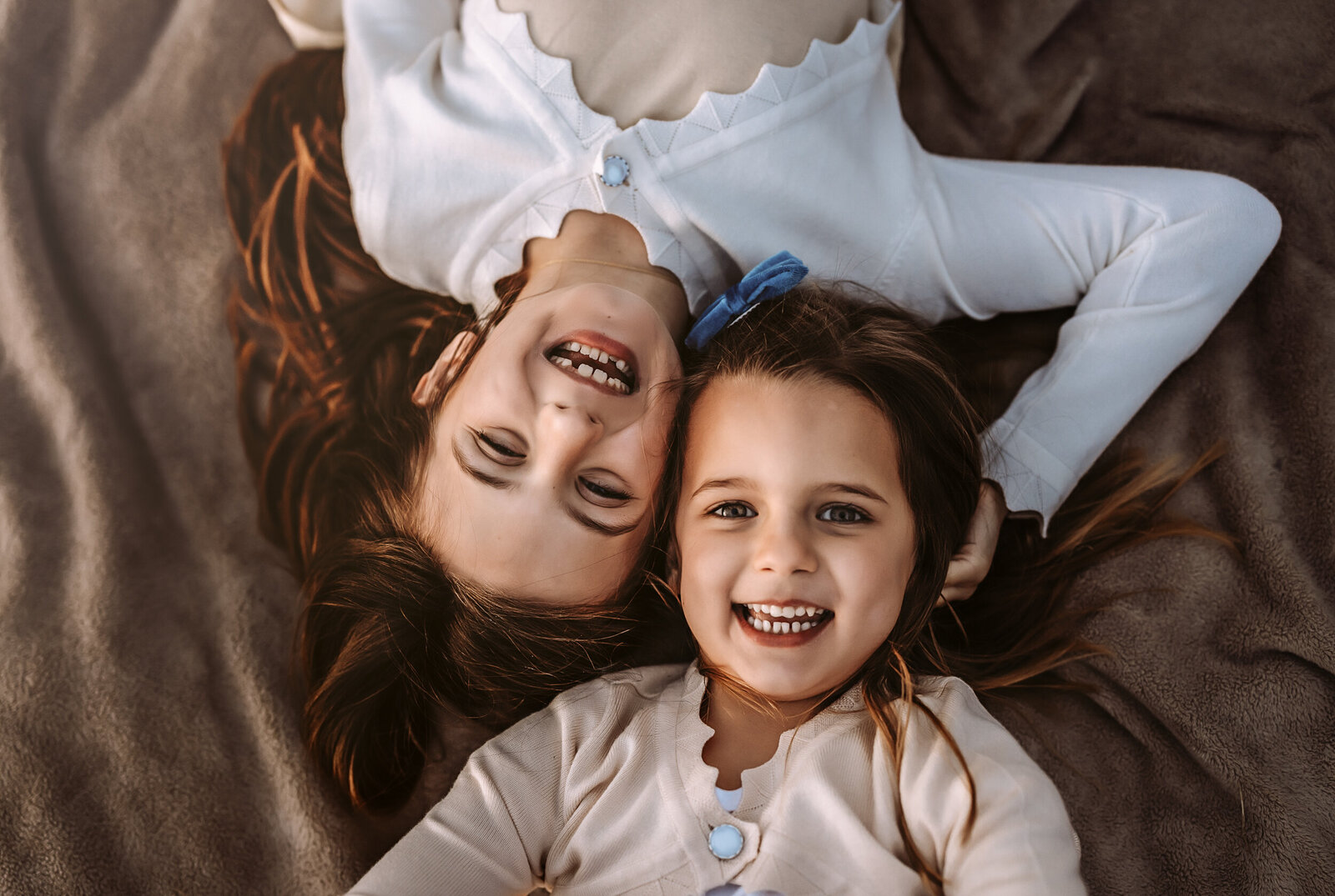 Two little girls laying on a blanket with heads next to each other laying in opposite direction smiling looking up.