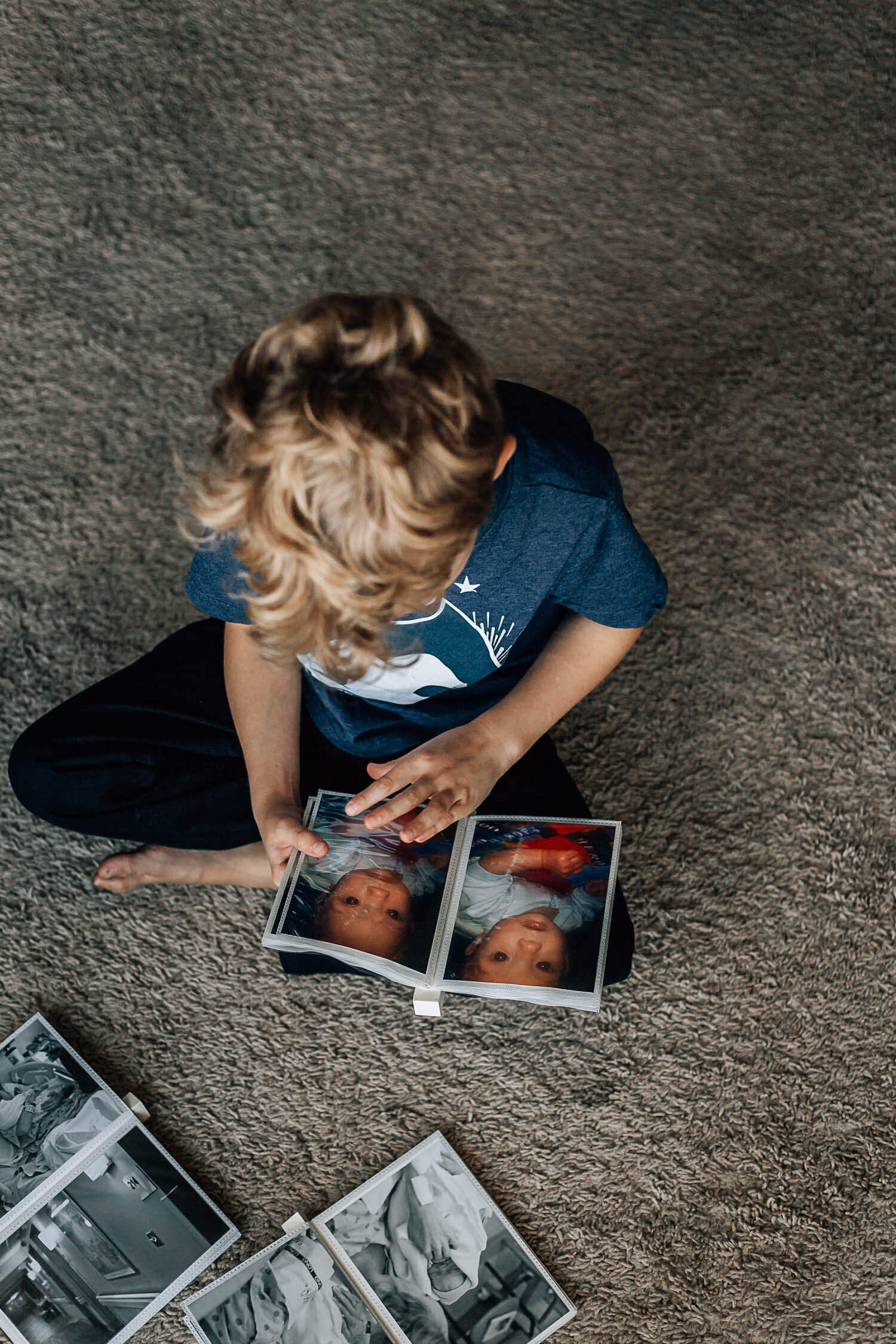 Hampton Roads Photographers family photos with little boy with curly blonde hair sitting criss cross on the floor looking at family photos in a photo album in Hampton Roads Virginia