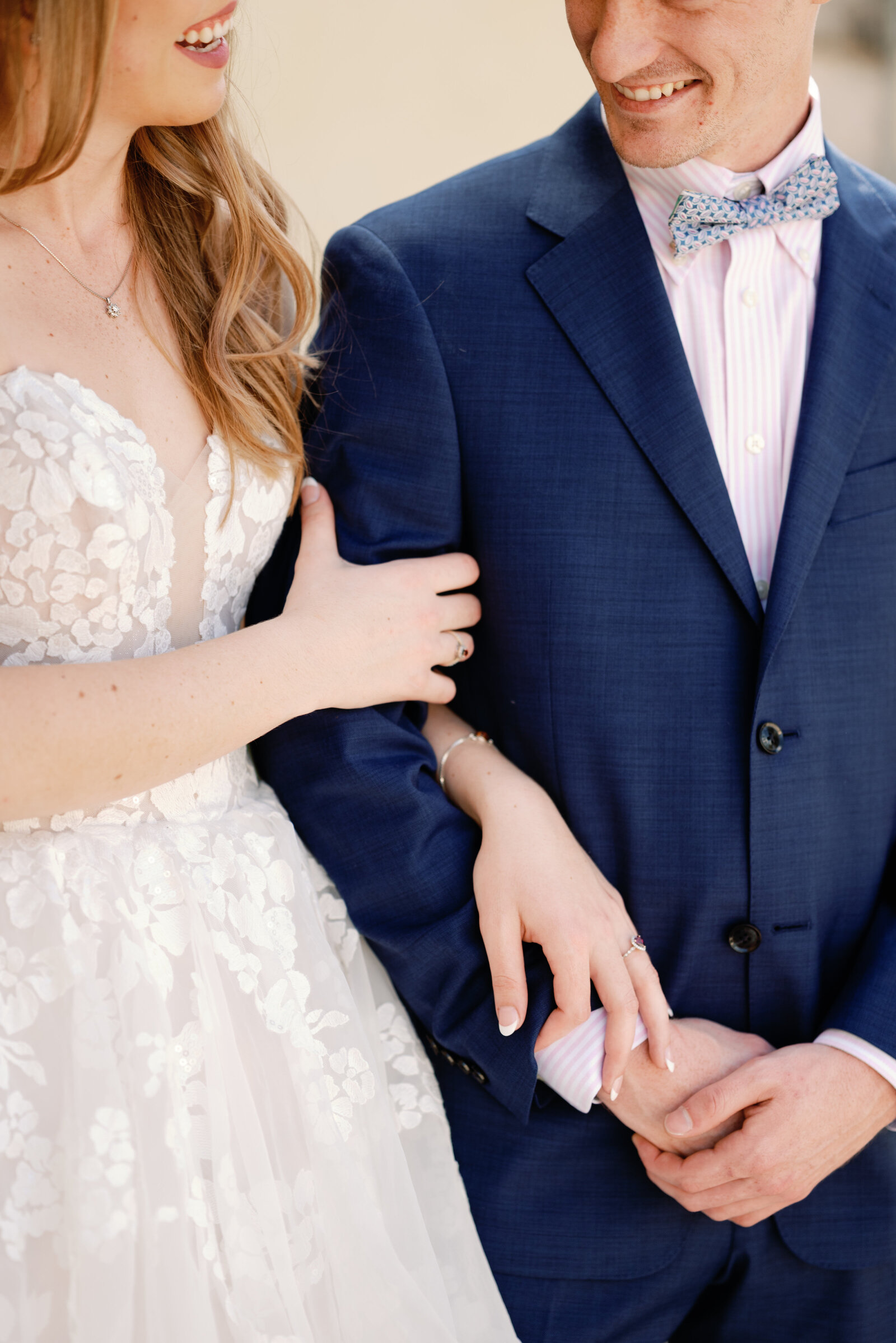 Close up of bride and grooms arms and hands together. Smiles on their faces