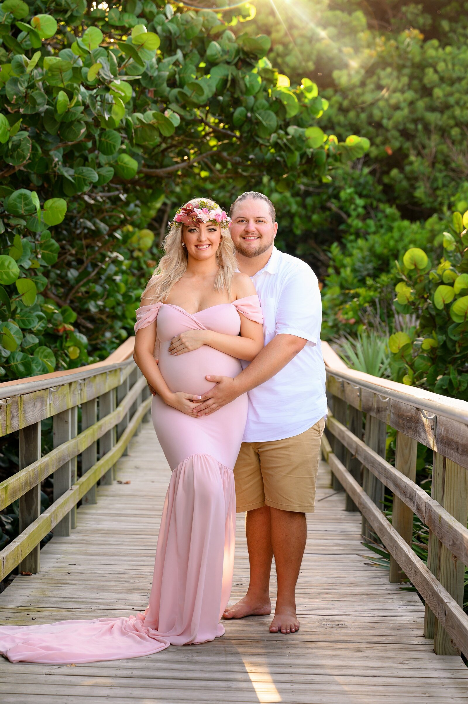 Husband and wife posed with baby bump on a boardwalk in Jupiter Florida beach