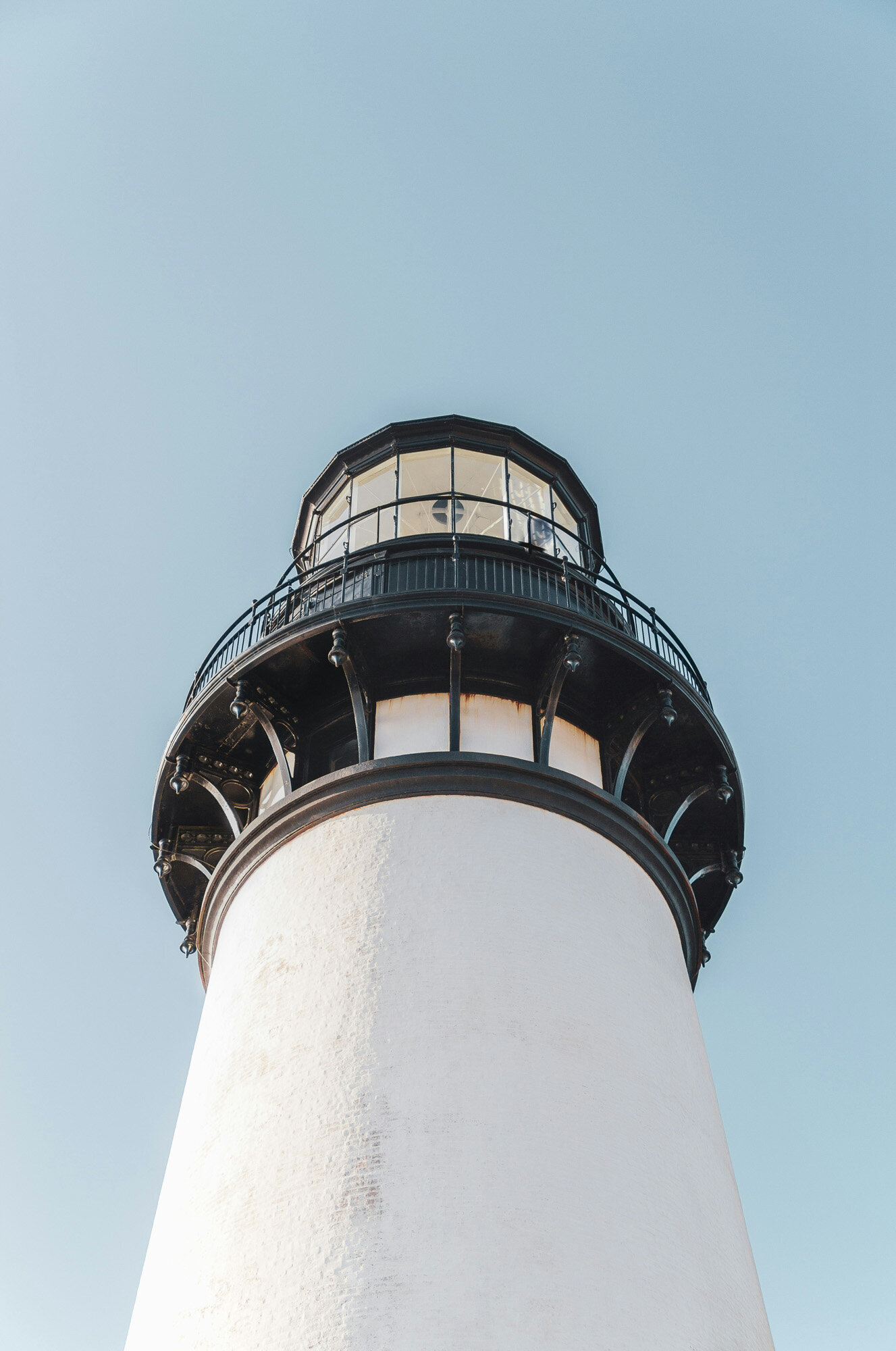 tall, white lighthouse tower with a black observation deck and lantern room stands against a clear, blue sky